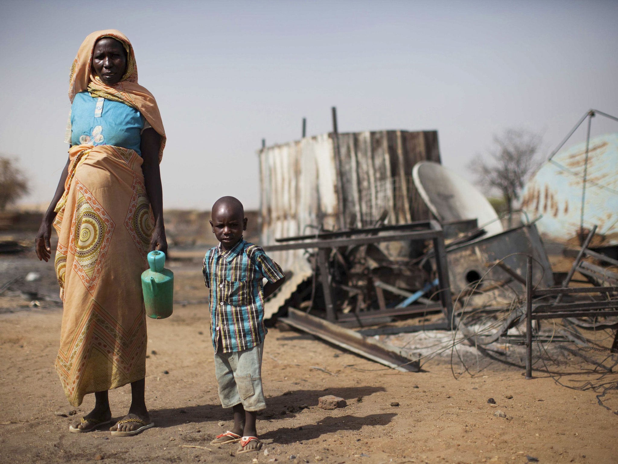 A displaced mother and her child inspect the remnants of their burnt house in Khor Abeche, South Darfur