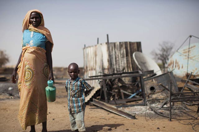 A displaced mother and her child inspect the remnants of their burnt house in Khor Abeche, South Darfur 