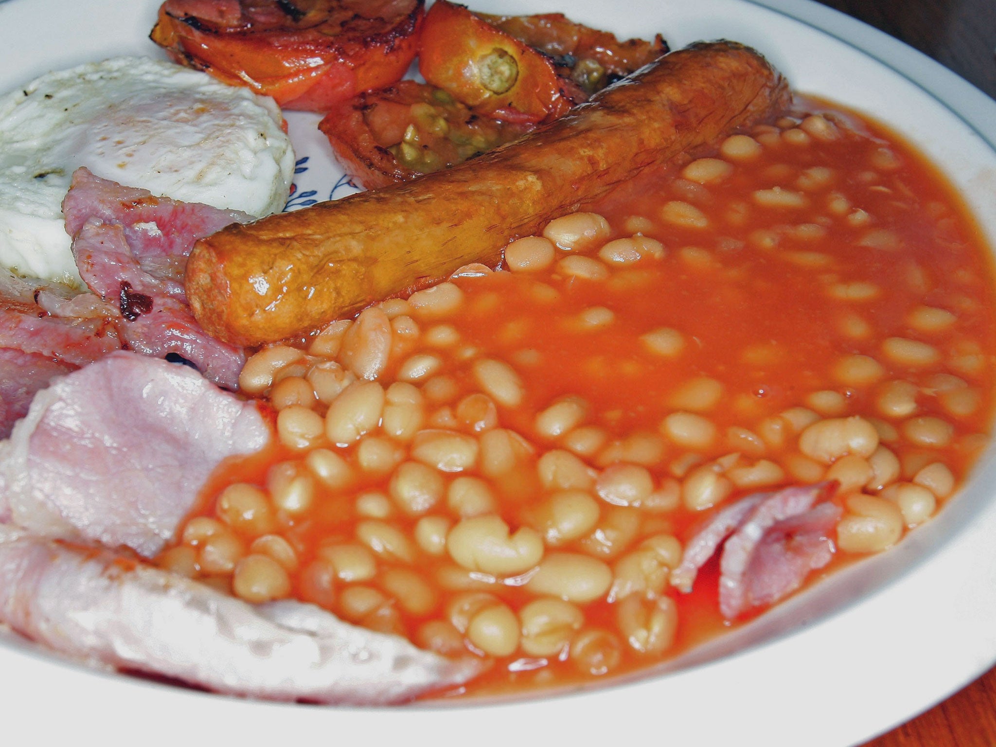 Baked beans are seen in a fried breakfast, along with rashers of bacon, a sausage, and an egg
