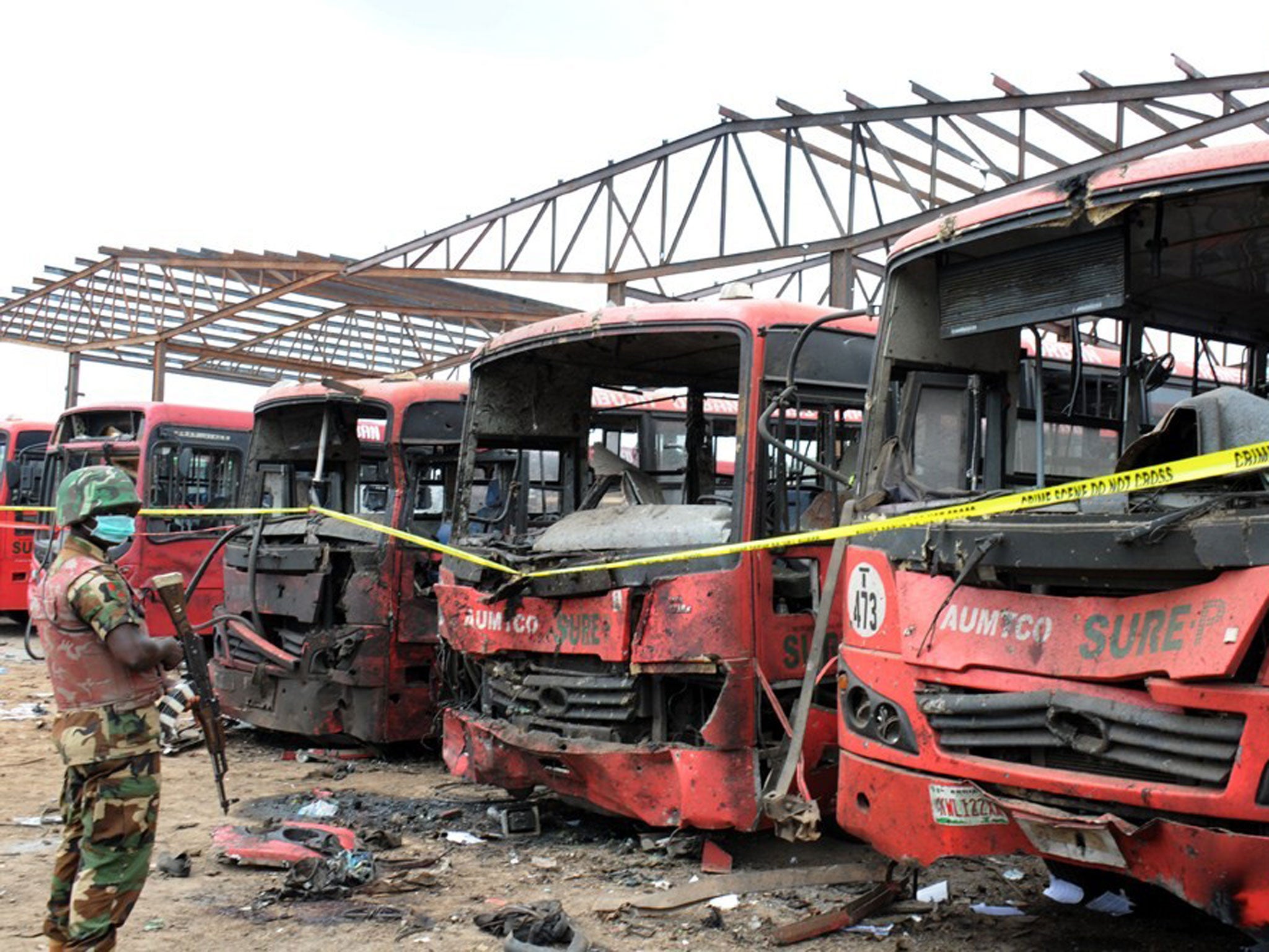 A soldier stands guard in front of burnt buses after an attack in Abuja. Twin blasts at a bus station packed with morning commuters on the outskirts of Nigeria's capital killed dozens of people, in what appeared to be the latest attack by Boko Haram Islam