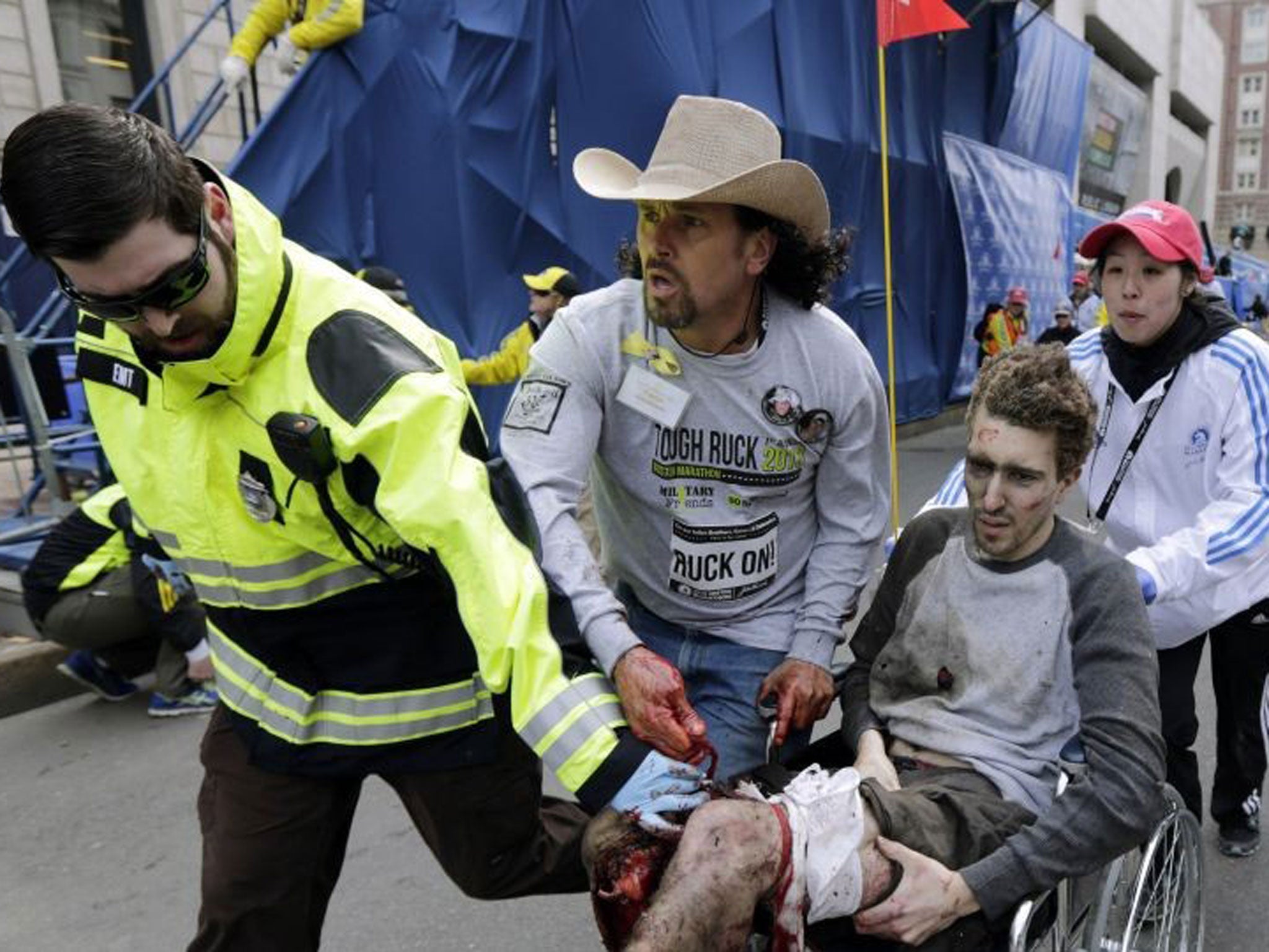 Paul Mitchell, left, bystander Carlos Arredondo, in cowboy hat, and Boston University student Devin Wang push Jeff Bauman in a wheelchair after he was injured in one of two explosions near the finish line of the Boston Marathon.