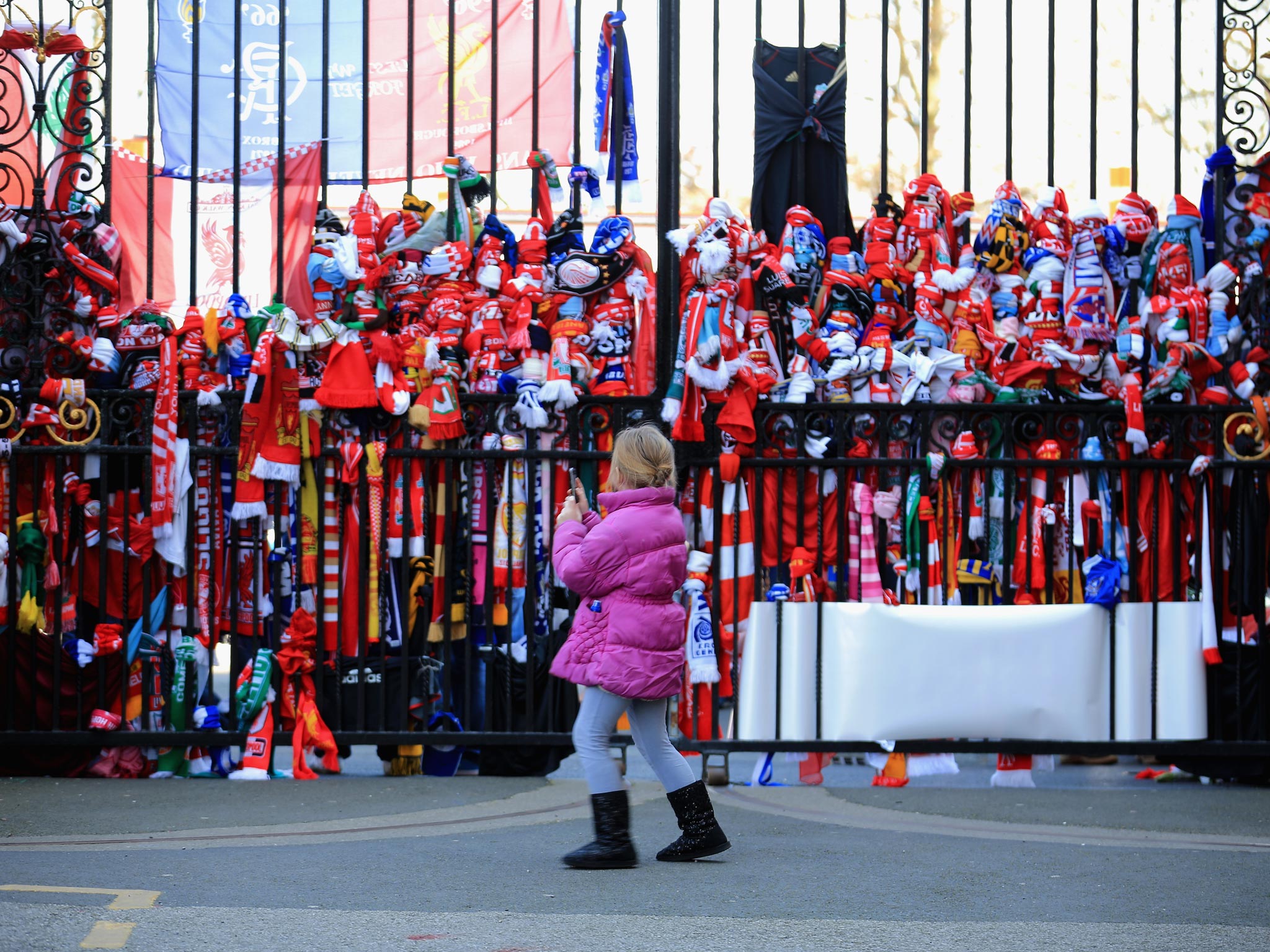 A girl stands outside the Anfield gates, covered in scarves and tributes to the 96 victims of the Hillsborough disaster