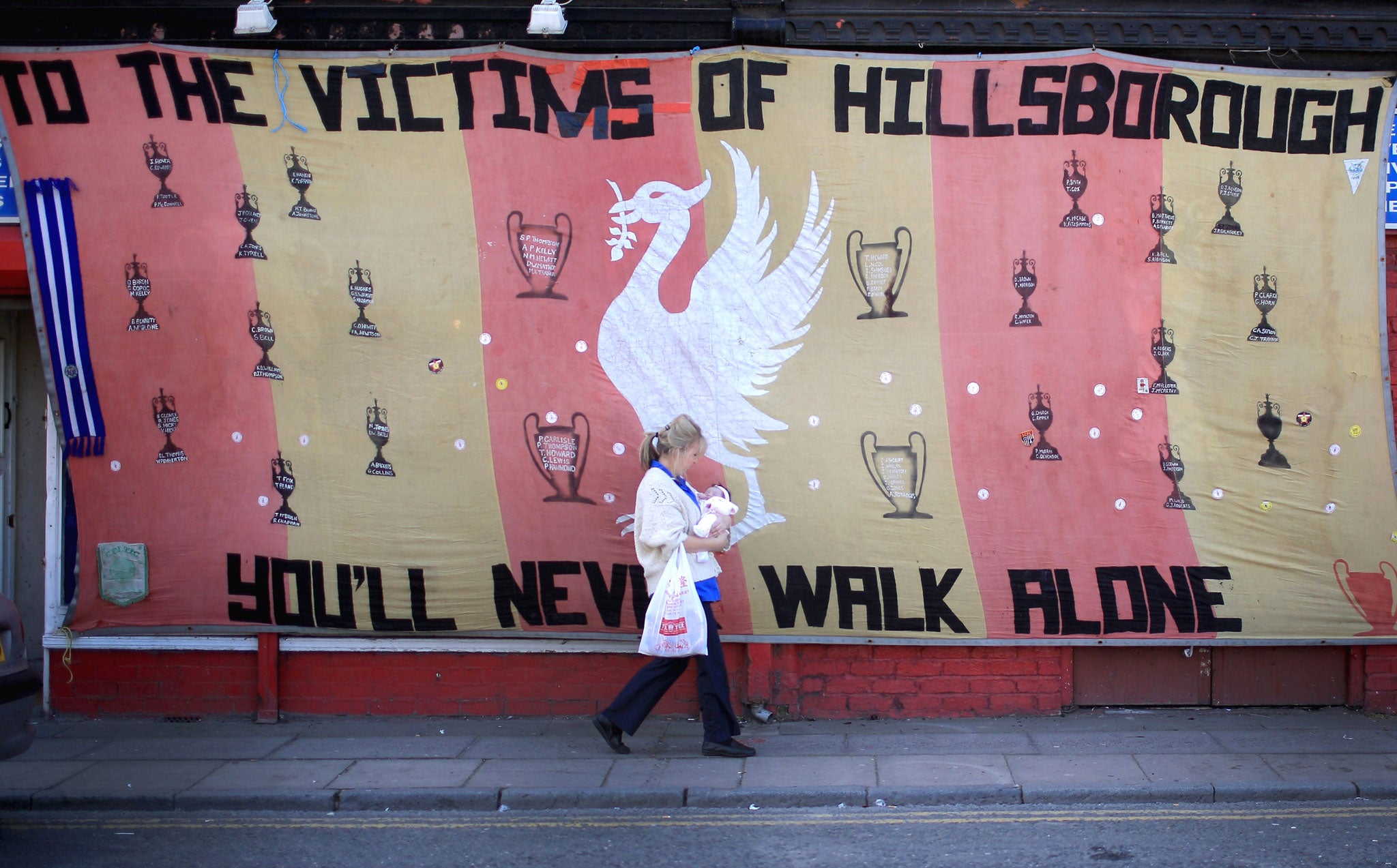 A woman walks past a Hillsborough tribute banner as fans arrive in Anfield for a memorial service marking the 25th anniversary of the Hillsborough Disaster at Anfield stadium in Liverpool
