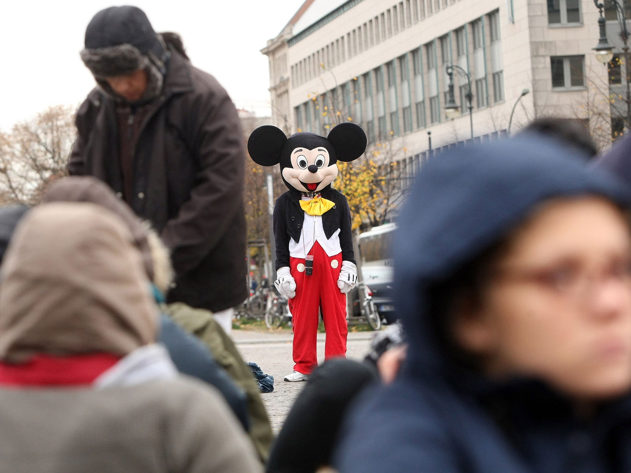 A street performer dressed as Mickey Mouse stands near Brandenburg Gate.