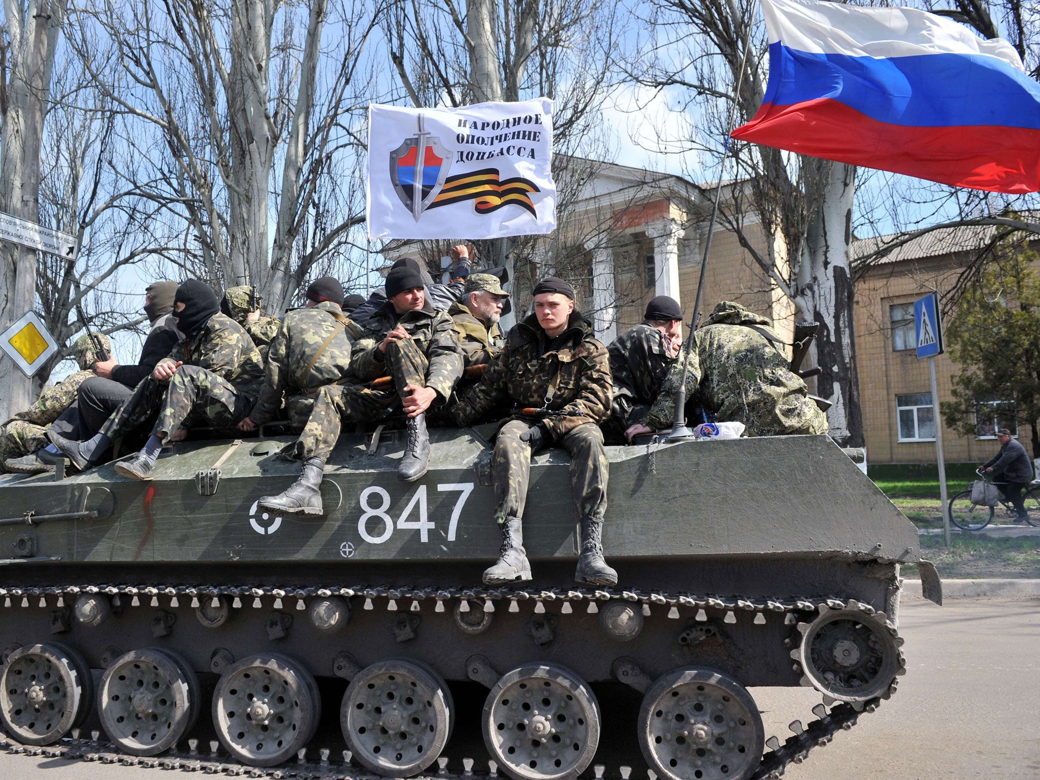 Men wearing military fatigues sit by a Russian flag and a white flag reading "People's volunteer corps of Donetsk" as they ride on an armoured personnel carrier (APC) in the eastern Ukrainian city of Slavyansk