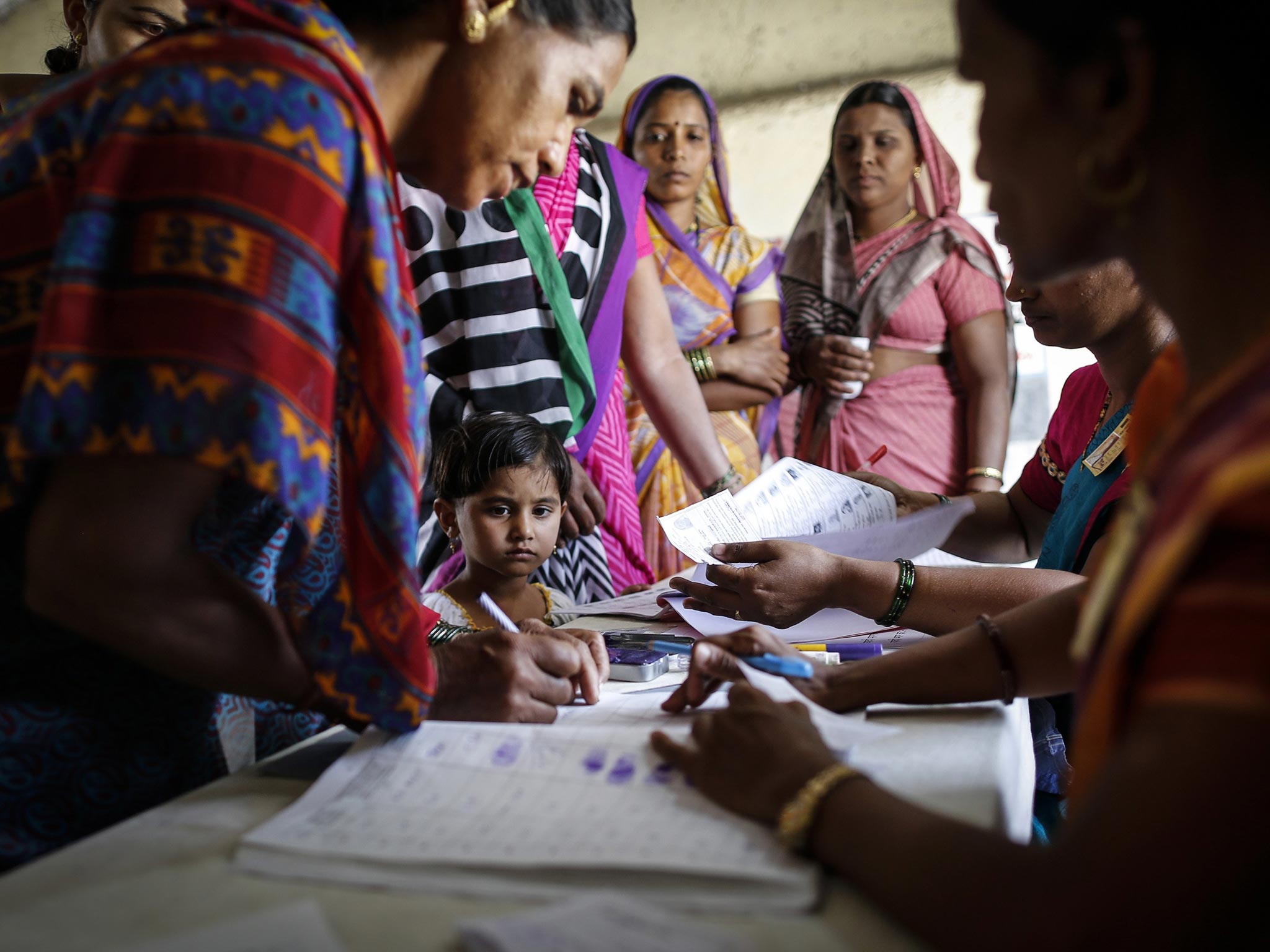A girl looks on as her mother signs before casting her vote at a polling station in the village of Shirgaon, India