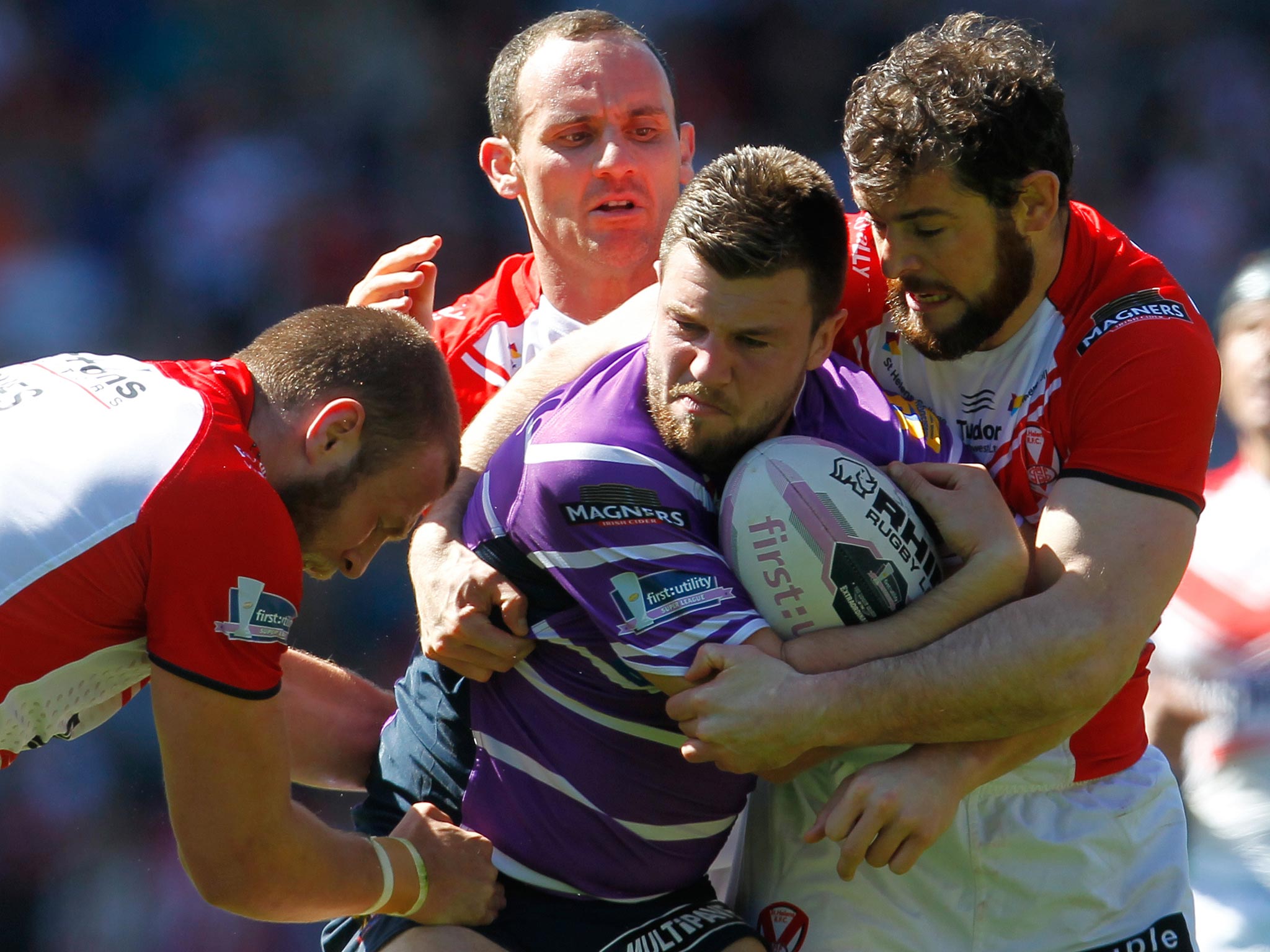 Darrell Goulding of Wigan is tackled by Josh Jones (L), Lance Hohaia and Paul Wellens (R) during the Super League match between St Helens and Wigan