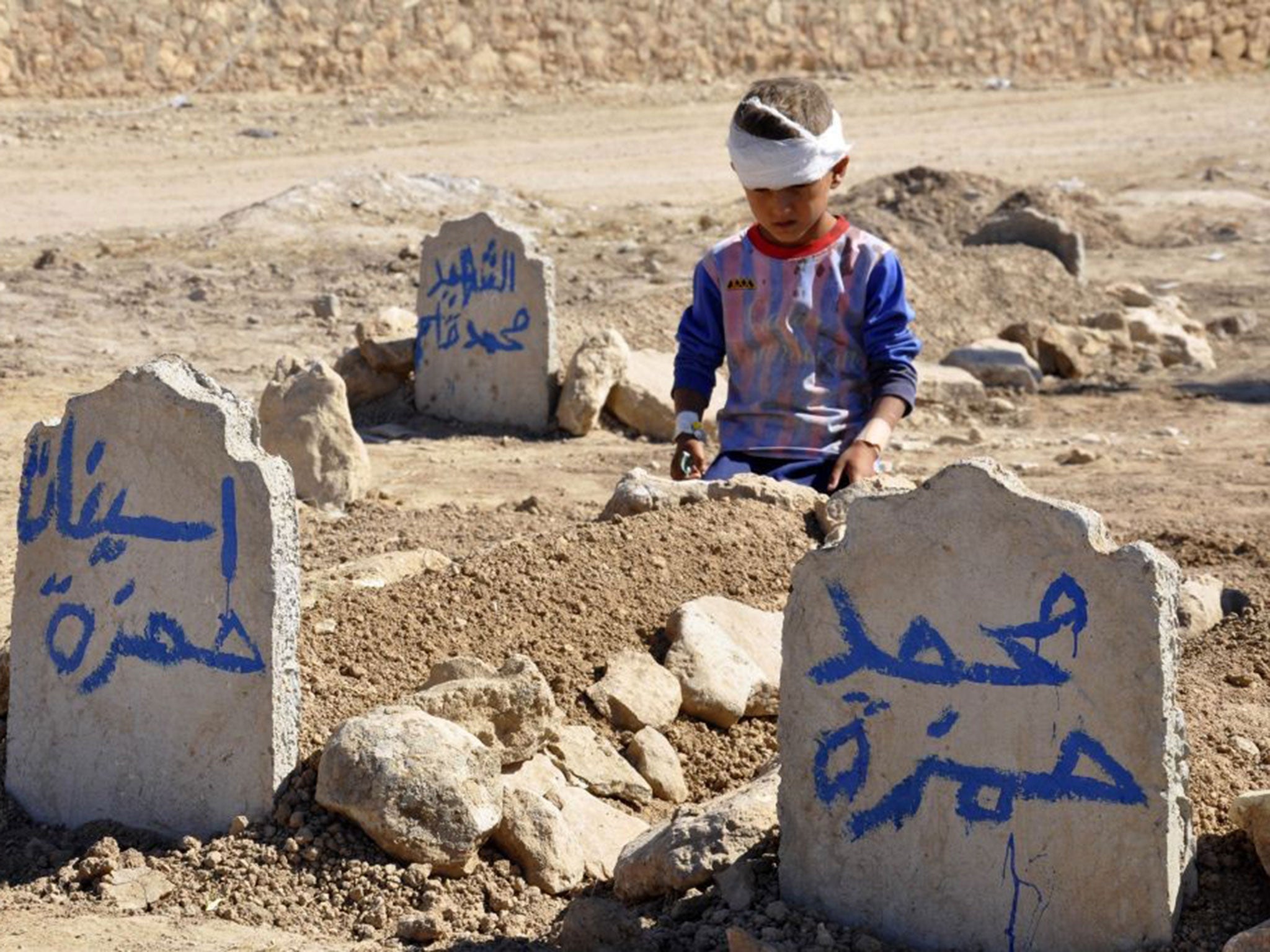 Ali Hamza, eight, sits at the grave of his brother, Mohammed, and sister Asinat, who were killed by an IED at their school in Qabak