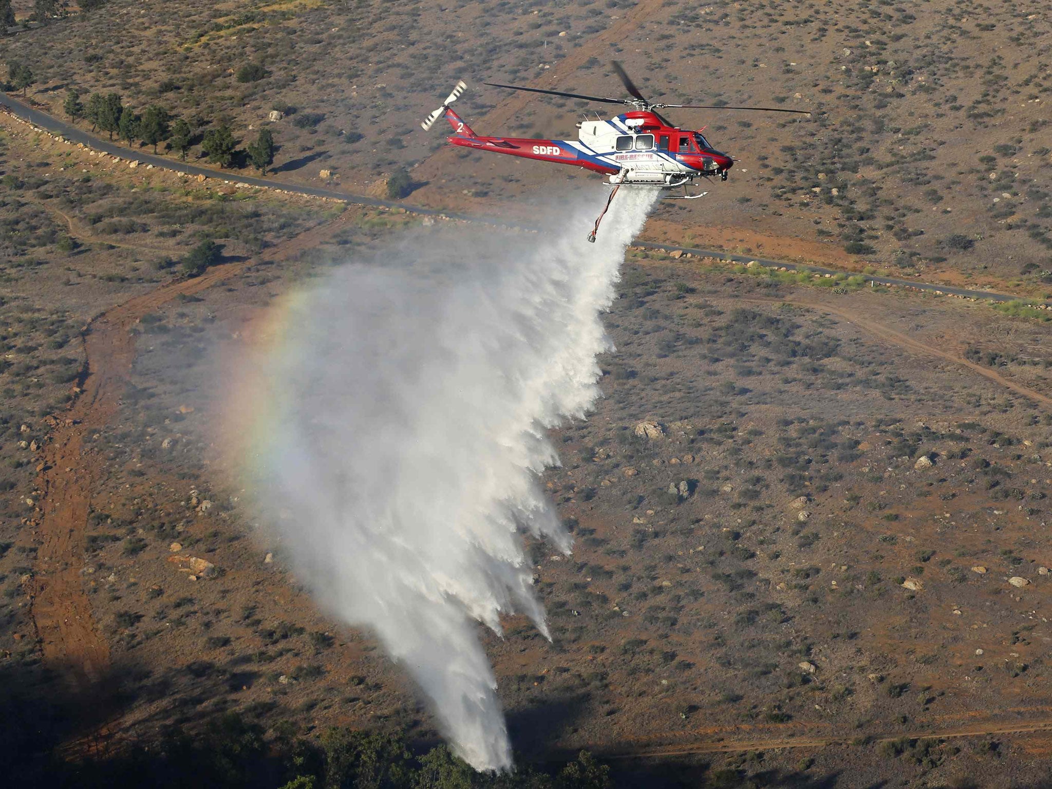 A helicopter drops water on a burning canyon next to homes as firefighters battle the Bernardo Fire, north of San Diego, California