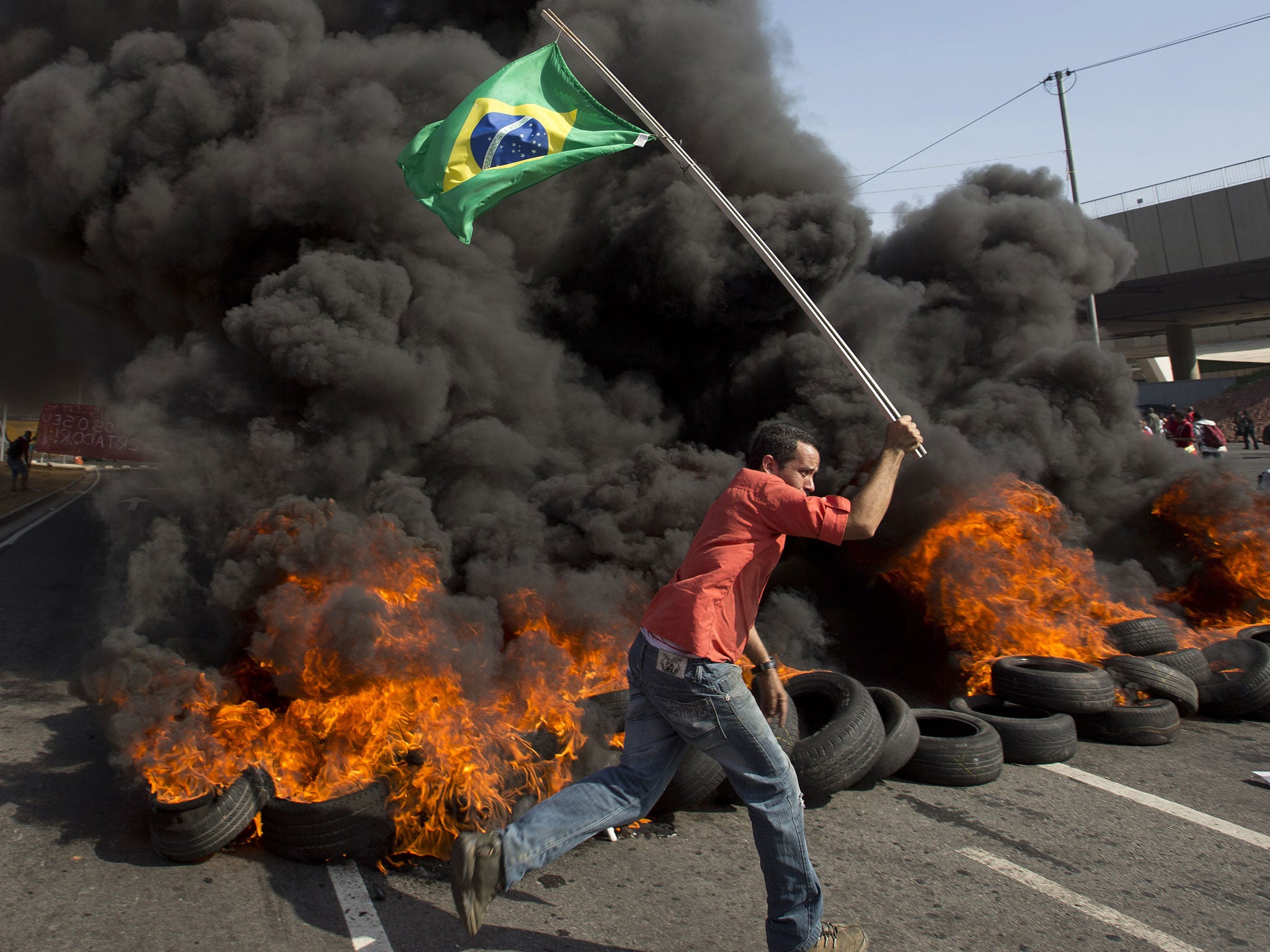 A member of the Homeless Workers Movement carries a Brazilian flag past burning tires during a protest against the money spent on the World Cup near Itaquerao stadium which will host the international soccer tournament's first match in Sao Paulo