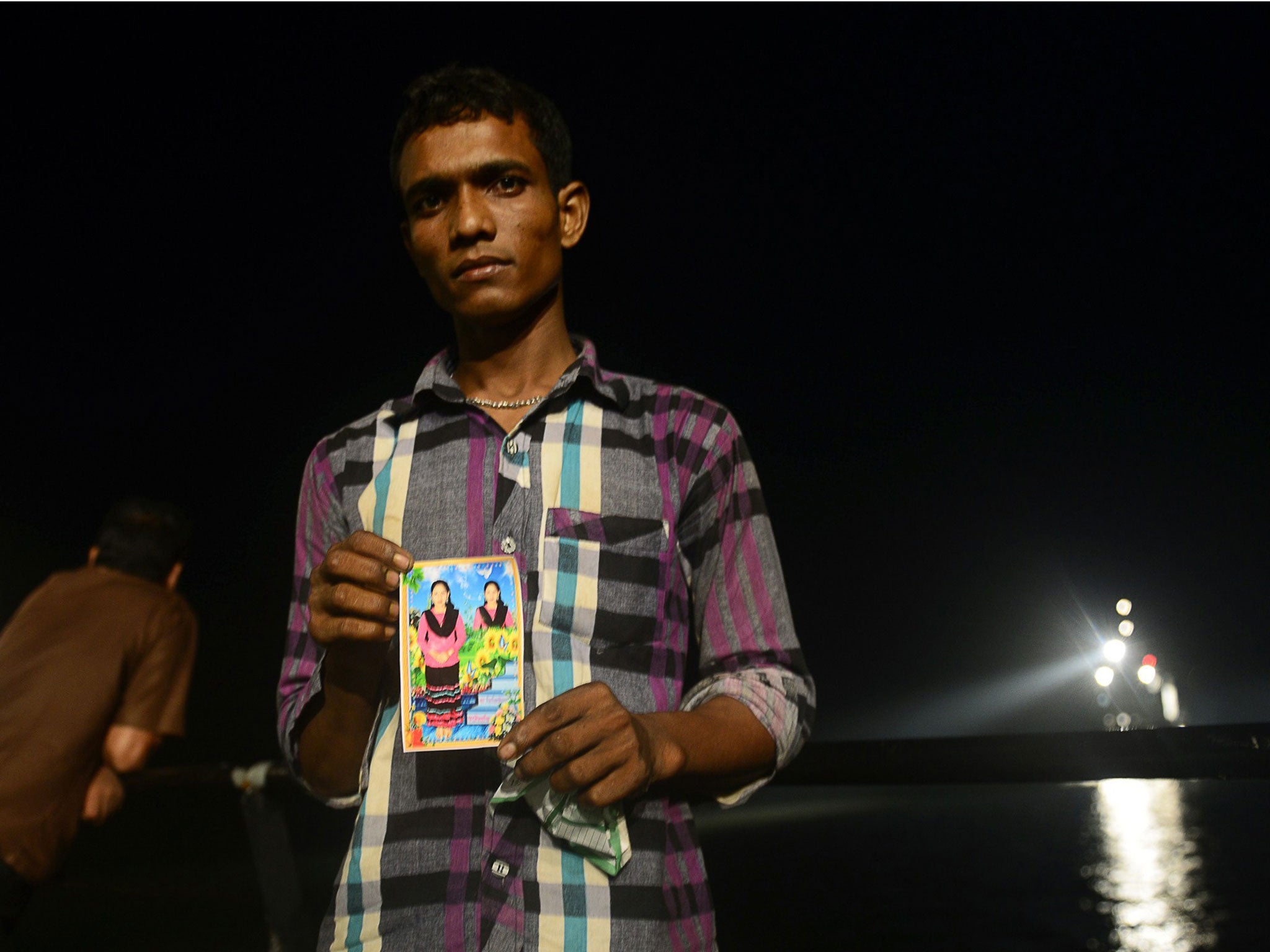 A Bangladeshi relative holds a photo of his missing niece during the night at the site where a ferry capsized and sank during bad weather on the Meghna river in the Munshiganj district