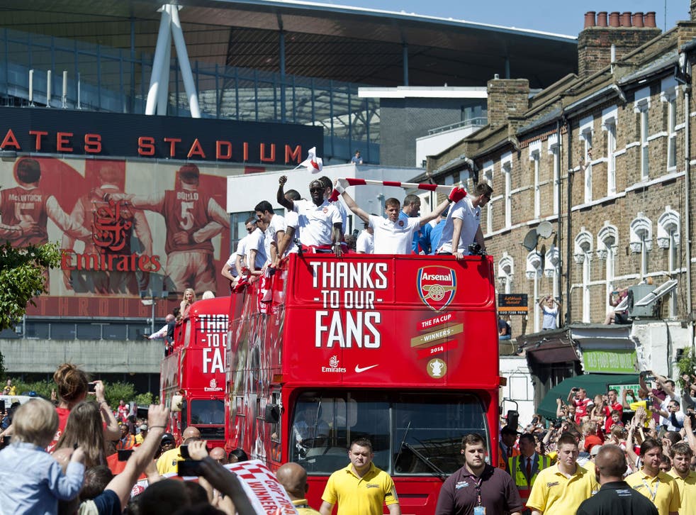 Arsenal players wave to fans from the top of an open topped bus as their victory parade leaves the Emirates stadium