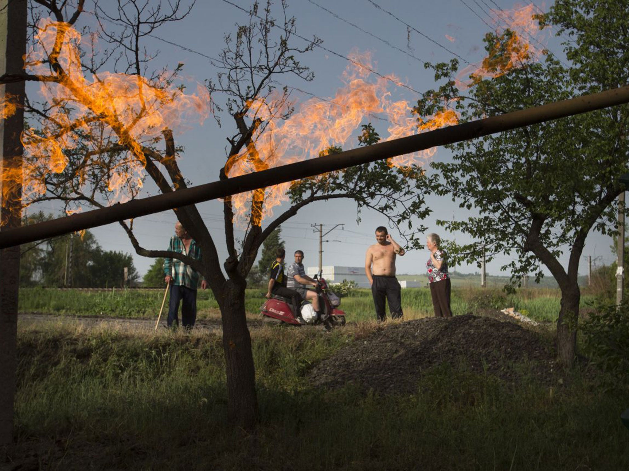 Residents watch flames from a gas pipe damaged by a mortar bomb during fighting in Slovyansk