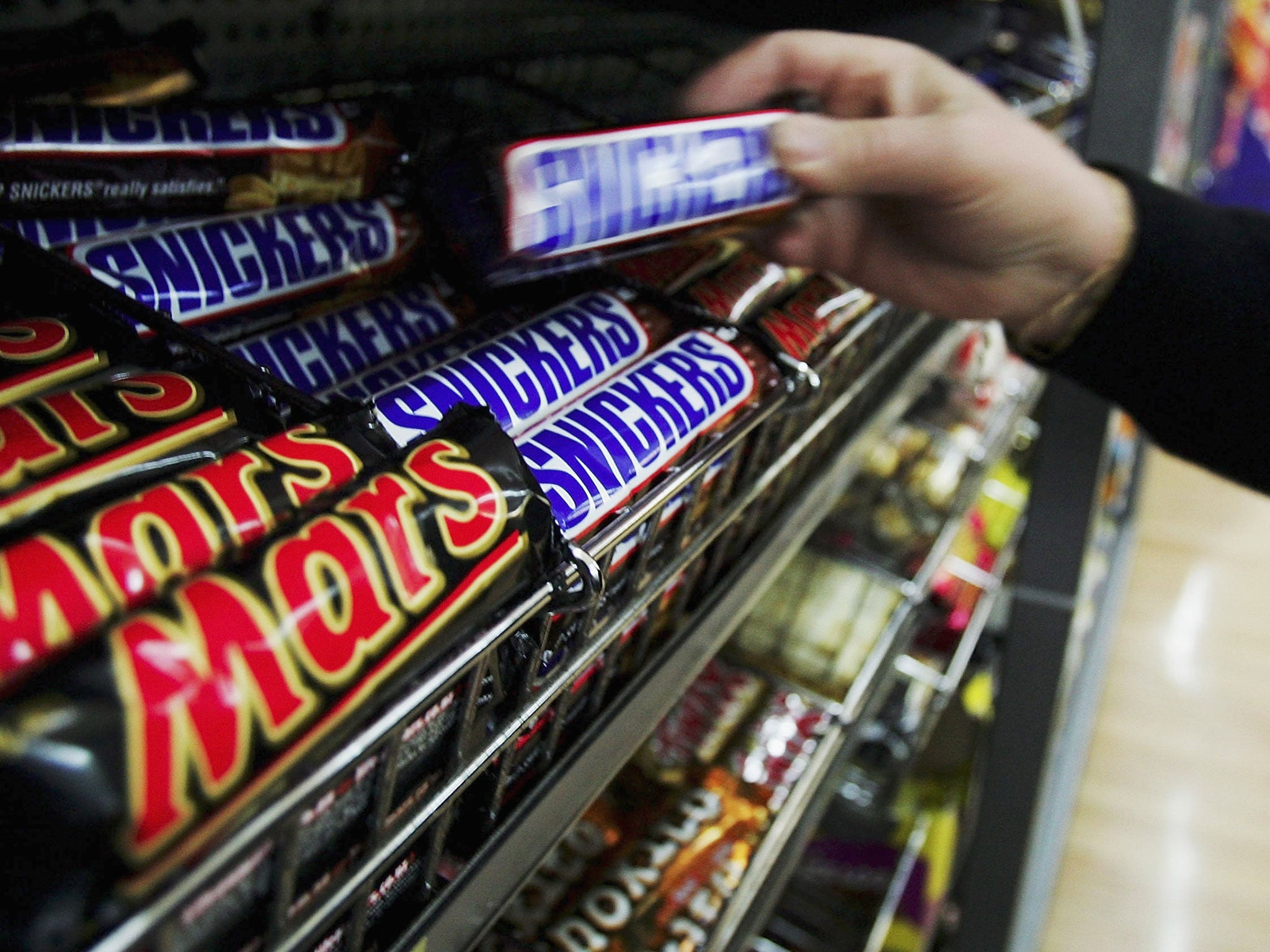 A customer picks up a Snickers Bar in a supermarket