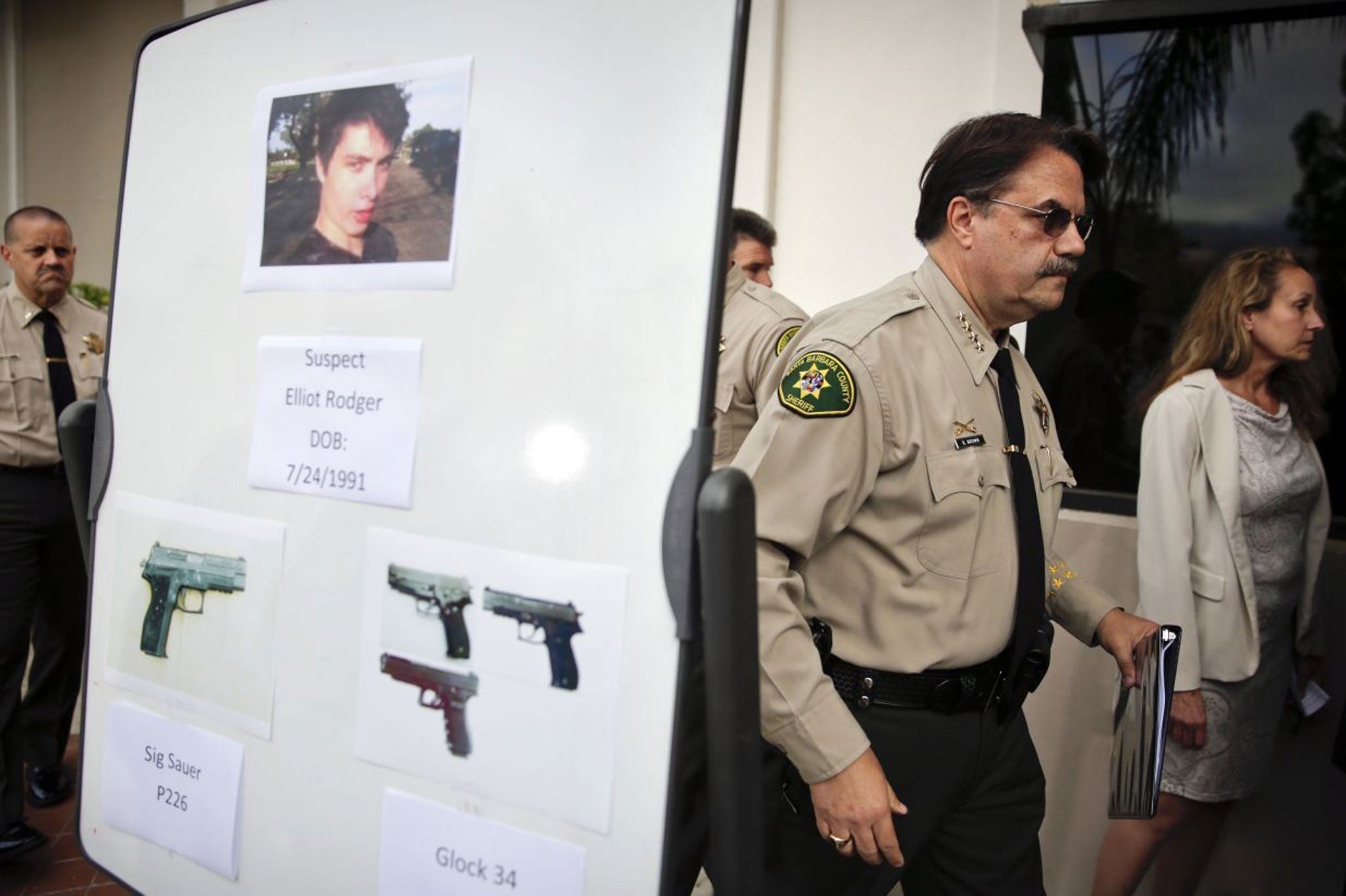 Santa Barbara County Sheriff Bill Brown, right, walks past a board showing the photos of suspected gunman Elliot Rodger and the weapons he used in Friday night's mass shooting