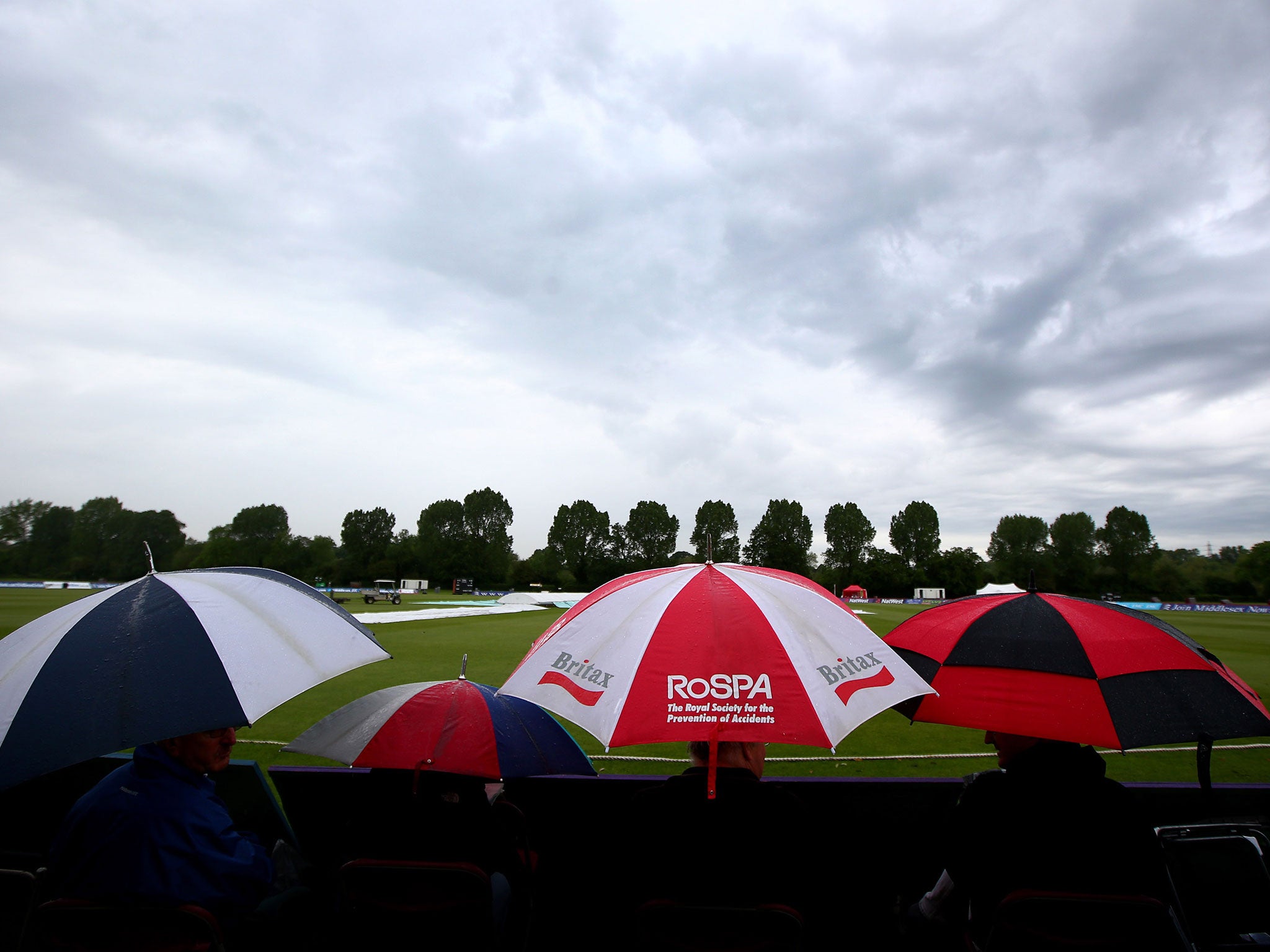 Spectators take shelter as the rain covers come on and the start of play is delayed during the LV County Championship match between Middlesex and Sussex on 26 May in Northwood, England
