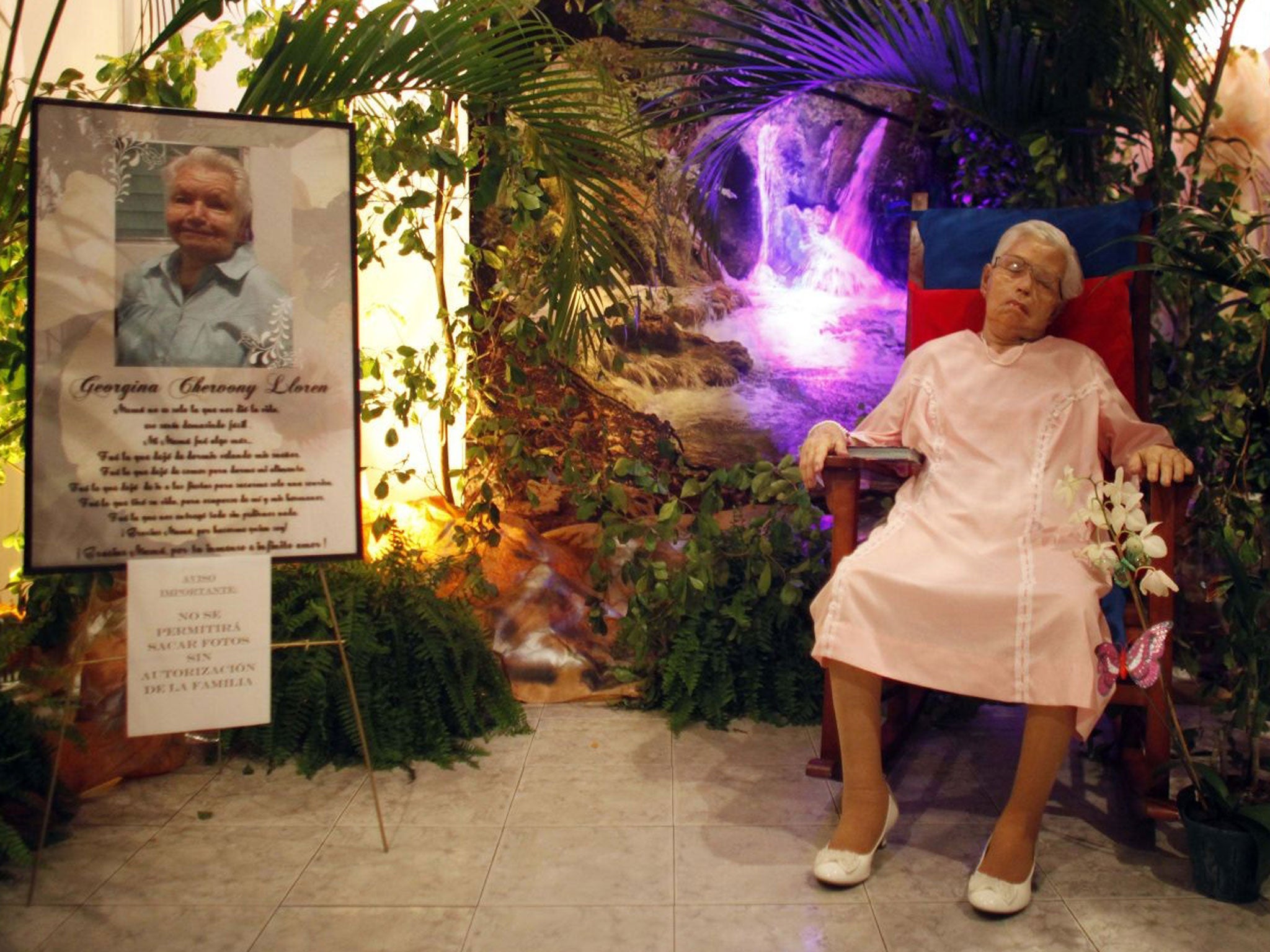 The body of Georgina Chervony Lloren, who died of natural causes on Sunday at the age of 80, is propped up in a rocking chair during her wake in a funeral home in San Juan, Puerto Rico, Monday, May 26, 2014.