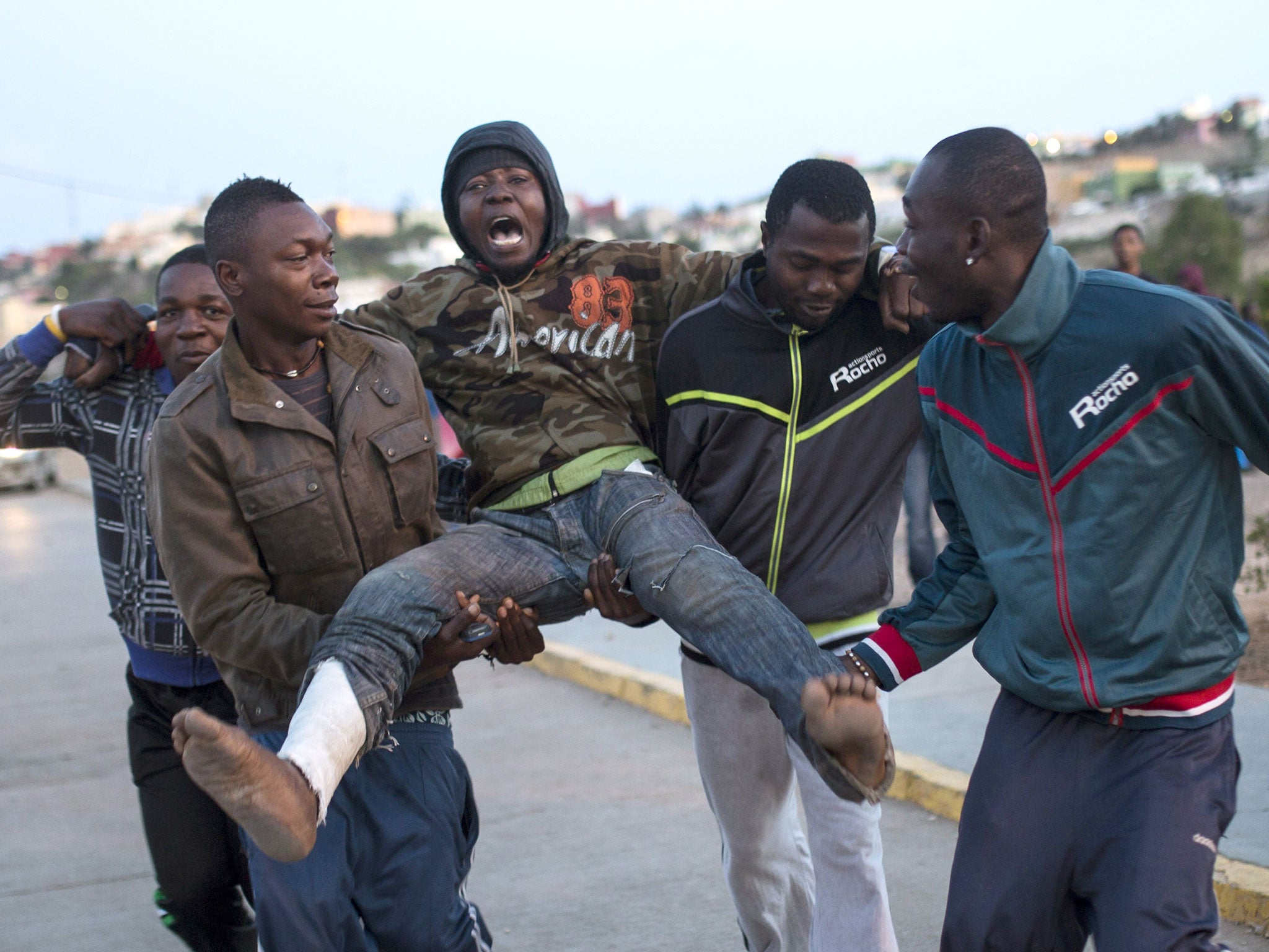 A wounded sub-Saharan migrant is helped by others as they arrive at a Temporary Centre for Immigrants (CETI) after scaling a metallic fence that divides Morocco and the Spanish enclave of Melilla