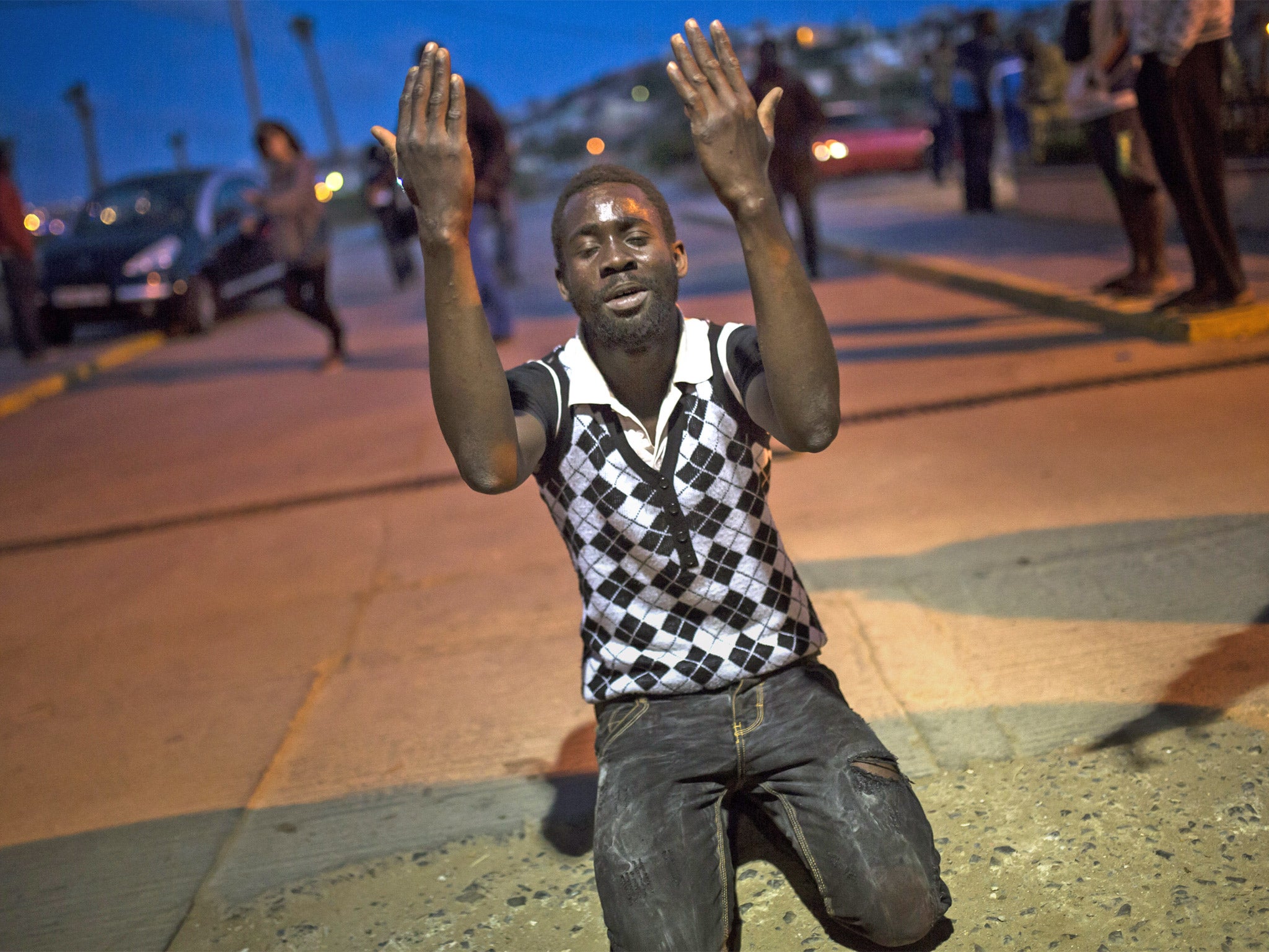 A migrant prays after scaling the metallic fence