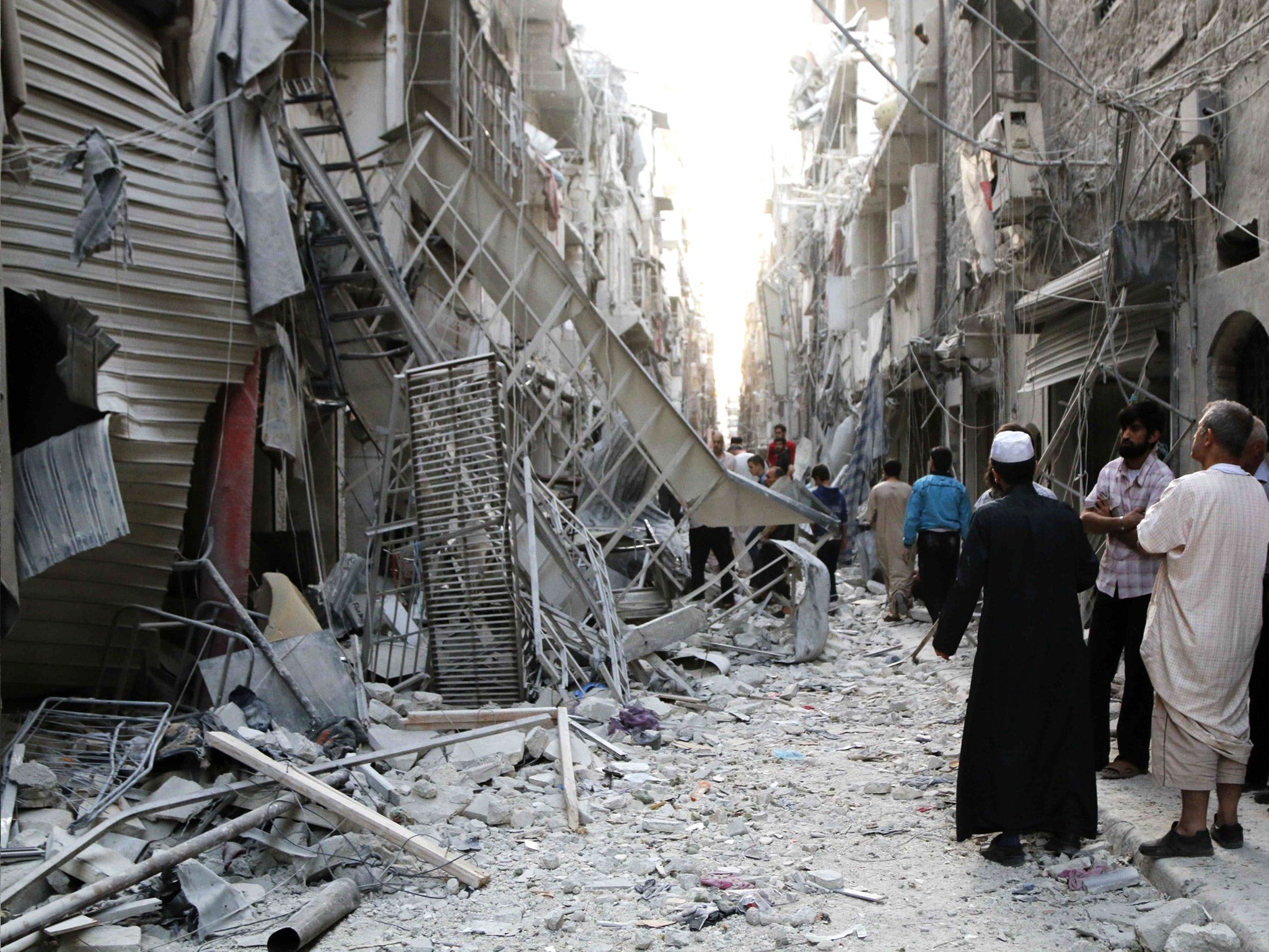 People stand near damaged buildings along a street at a site hit by what activists said was a barrel bomb dropped by forces loyal to Syria's President Bashar al-Assad in Aleppo