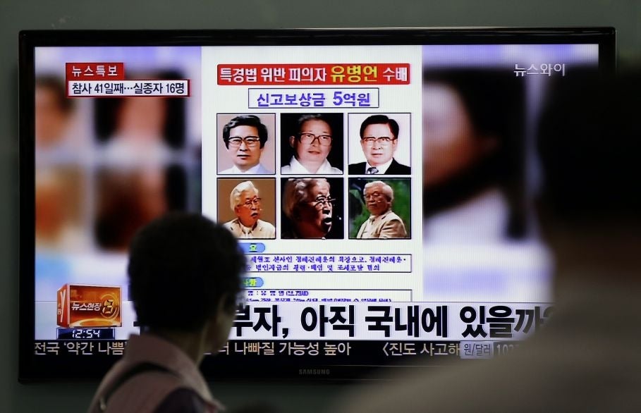 A woman watches a TV news program on the reward poster of Yoo Byung-eun at the Seoul Train Station in Seoul, South Korea