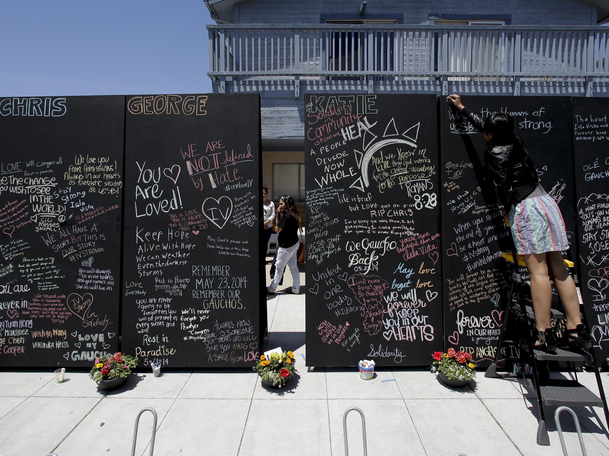 Rinda Sutrarhada (left) writes the names of victims
of last week’s mass shooting in Isla Vista, California, on a memorial wall near the scene
