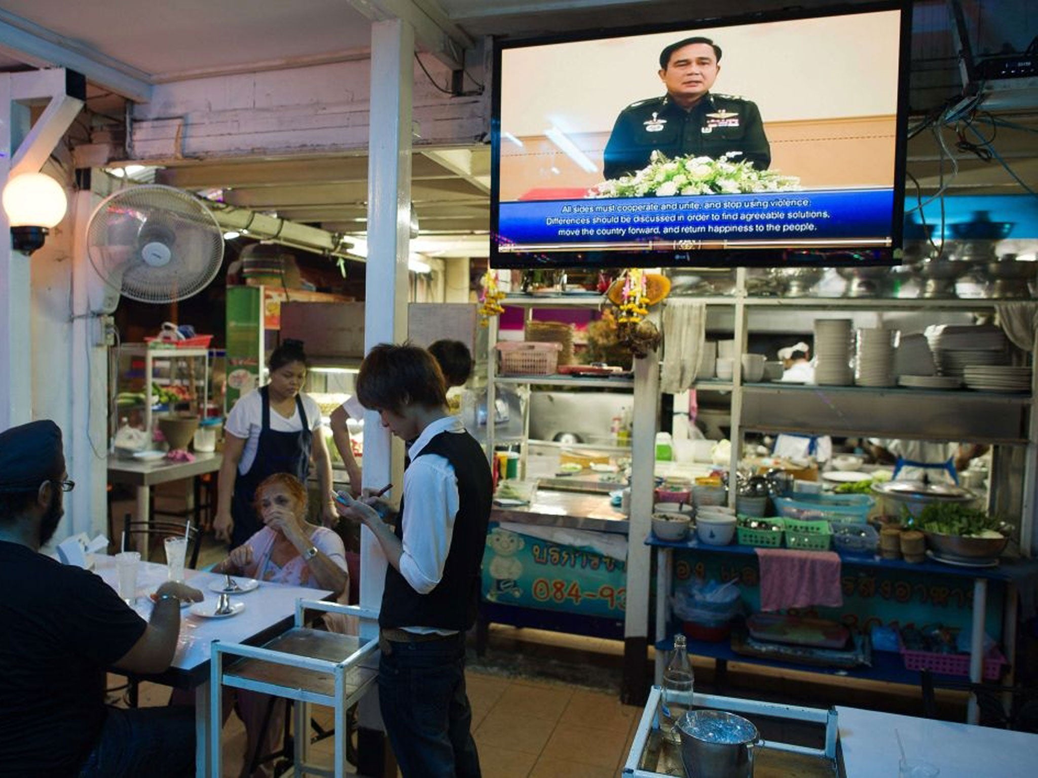Thai army chief General Prayut Chan-O-Cha (C) is seen making a speech on a television set as a waiter takes an order at a Thai restaurant in Bangkok on May 30, 2014. The European Union has voiced "extreme concern" about political detentions and censorship