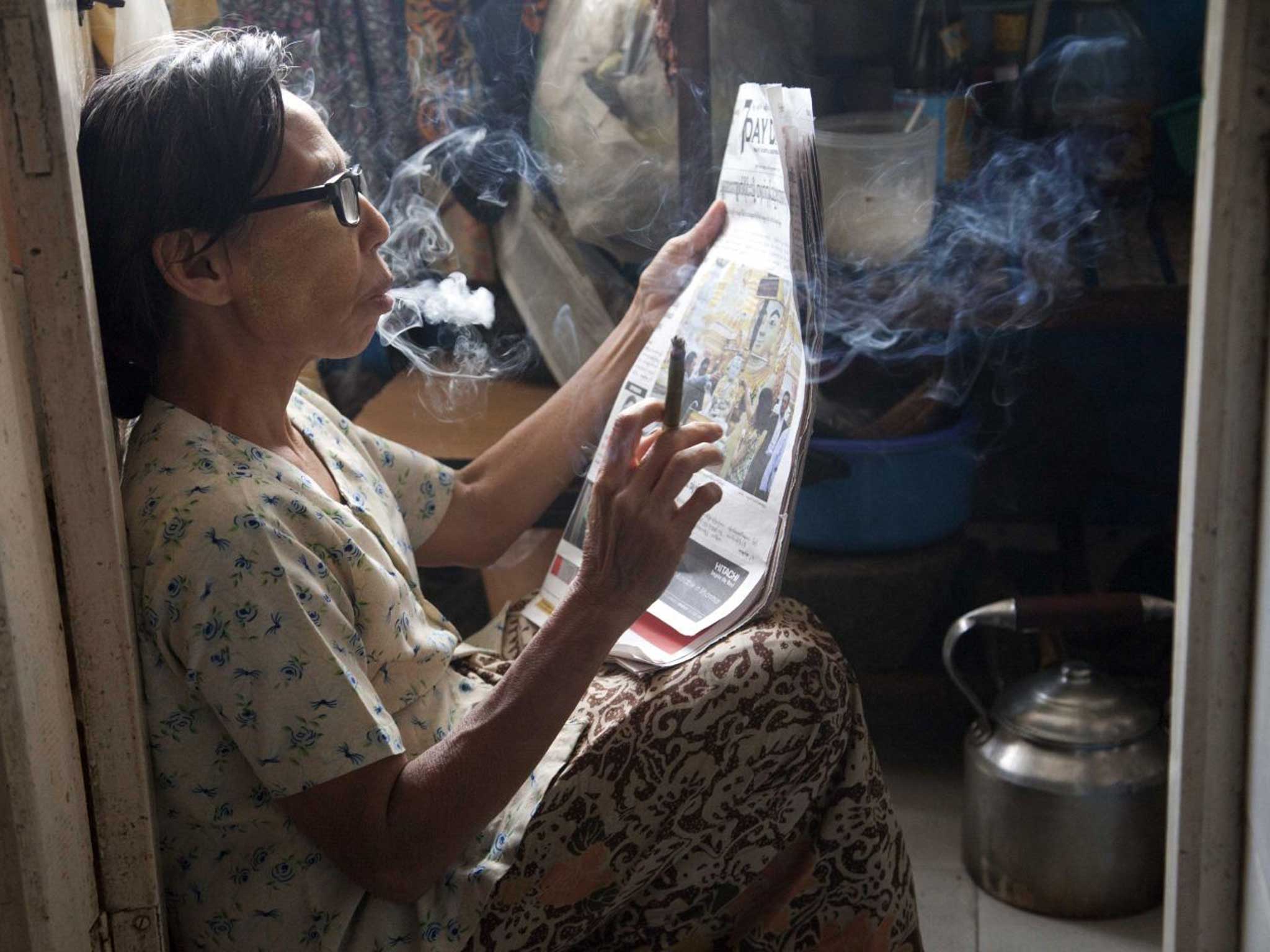 A woman in Burma reads the paper while smoking