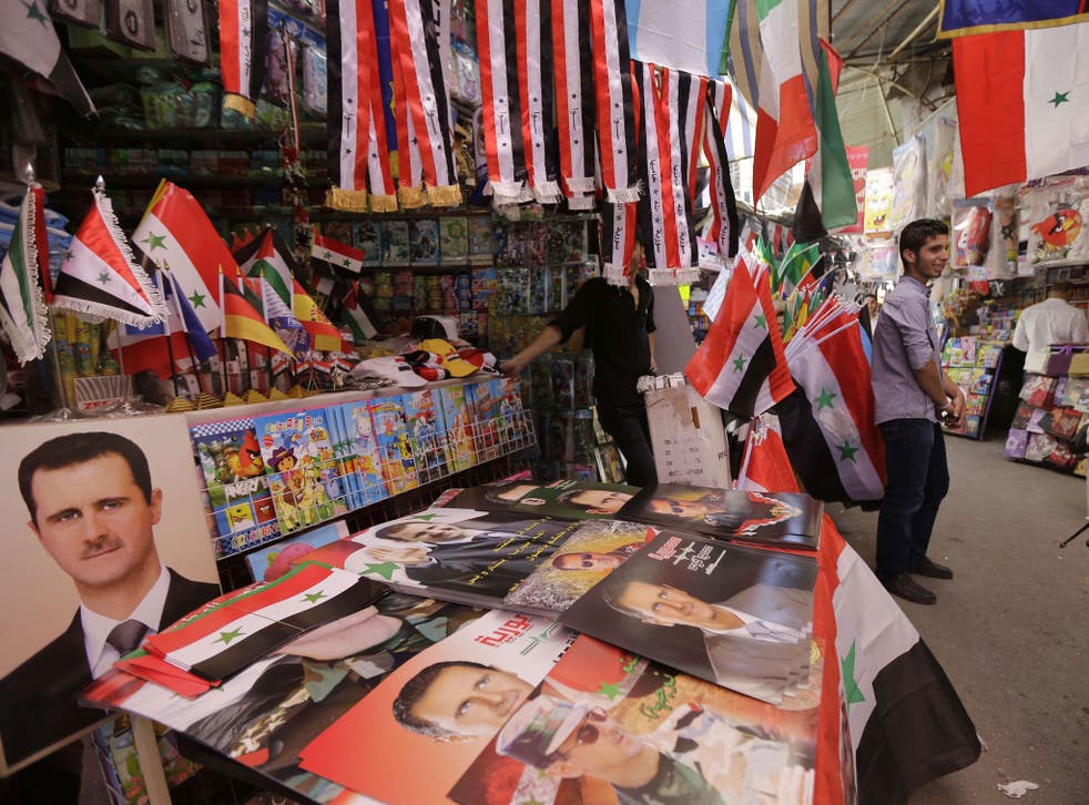 Syrians walk past campaign posters of Syrian President Bashar al-Assad displayed on a stall at a market on June 1, 2014 in the capital Damascus.