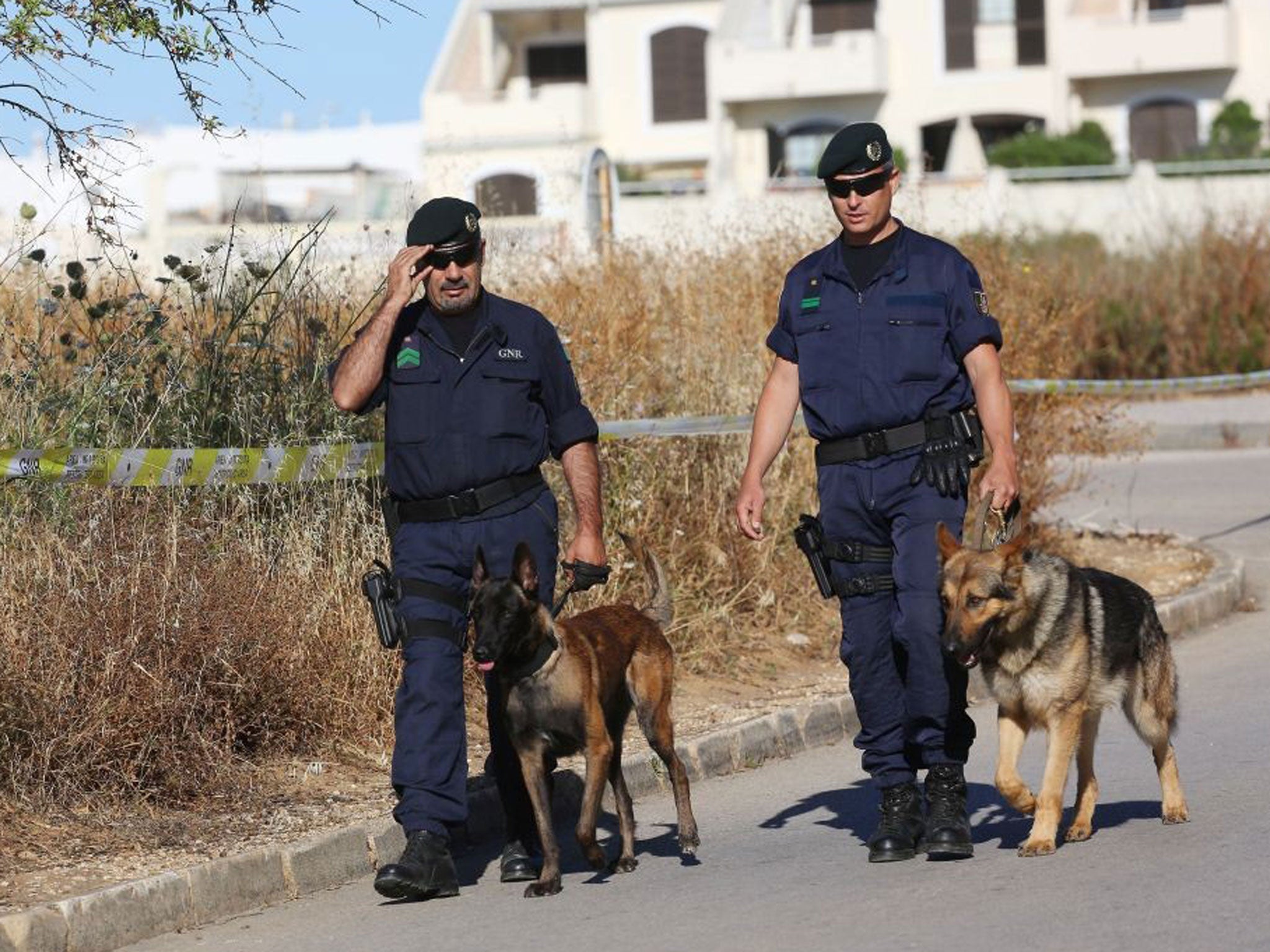 Portuguese police officers walk with dogs near a cordoned off area of scrubland close to where Madeleine McCann went missing seven years ago in the resort of Praia da Luz, Portugal, where where British police are currently searching