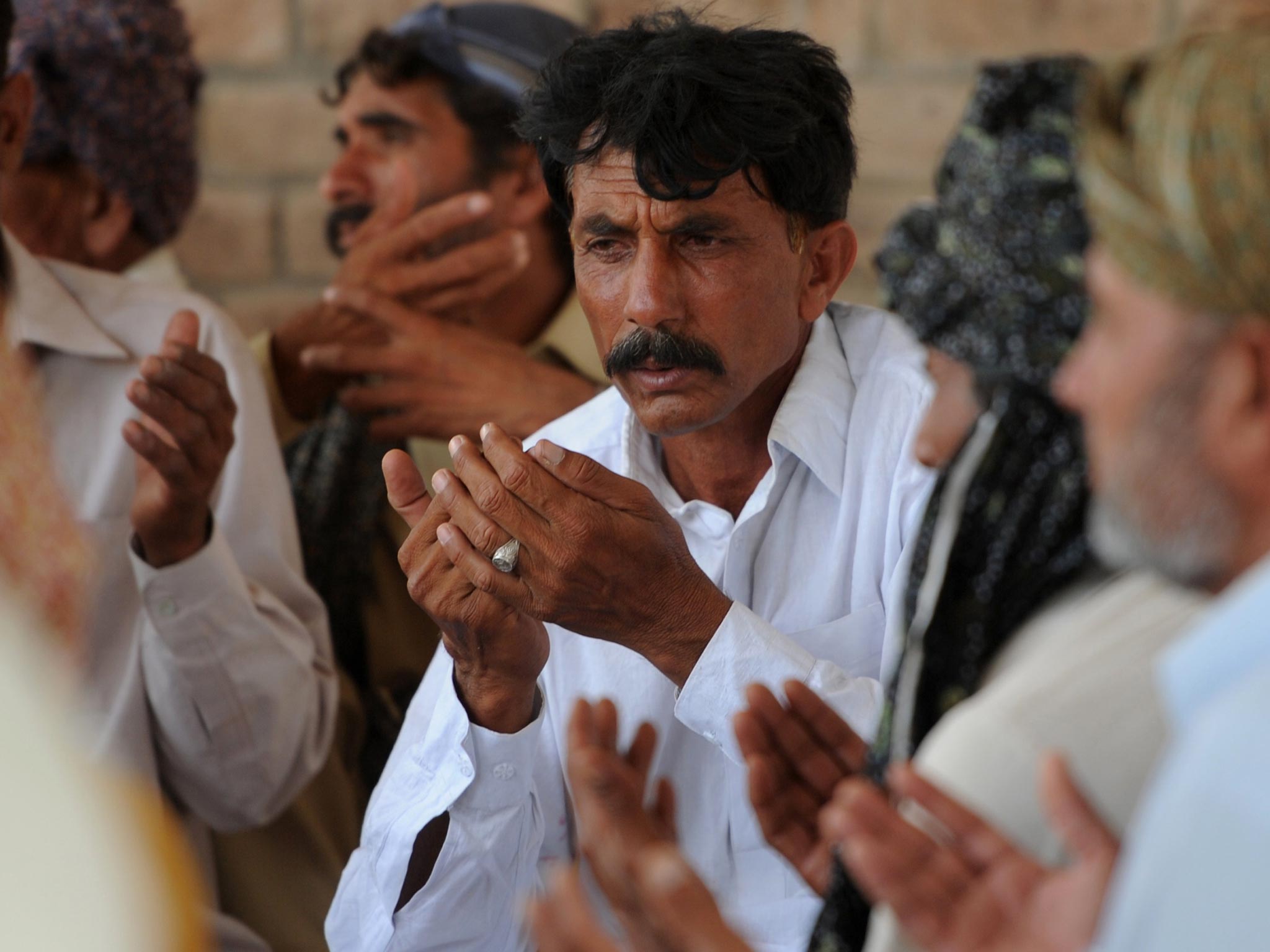 Pakistani resident Mohammad Iqbal (C) prays alongside relatives for his wife Farzana Parveen, who was beaten to death with bricks by her father and other family members
