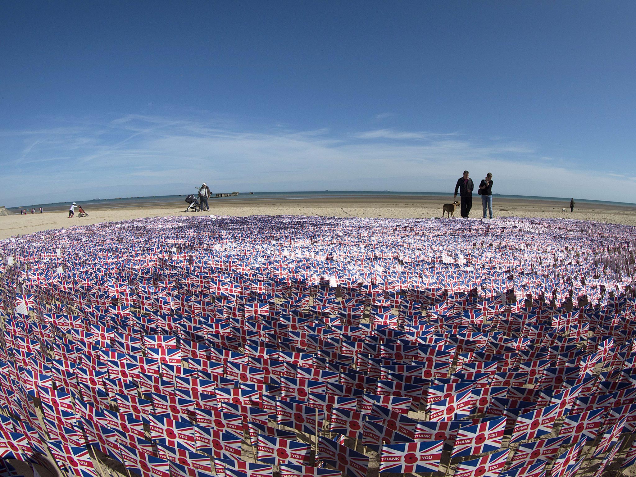 People walk along British national flags in Asnelles, Normandy
