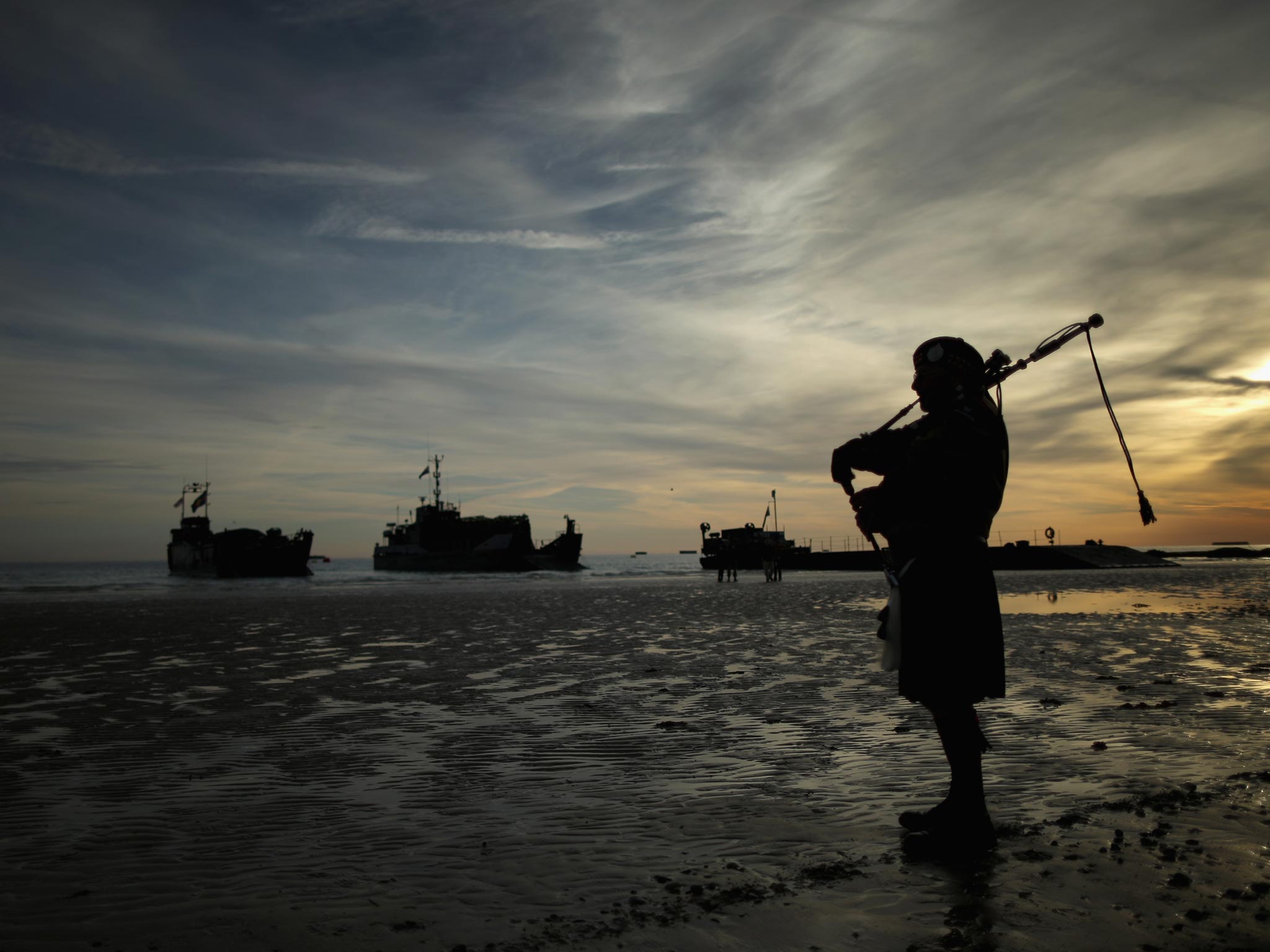 A piper plays a lament on Gold Beach as Royal Marines landing craft arrive at Arromanche at the start of yesterday’s D-Day commemorations