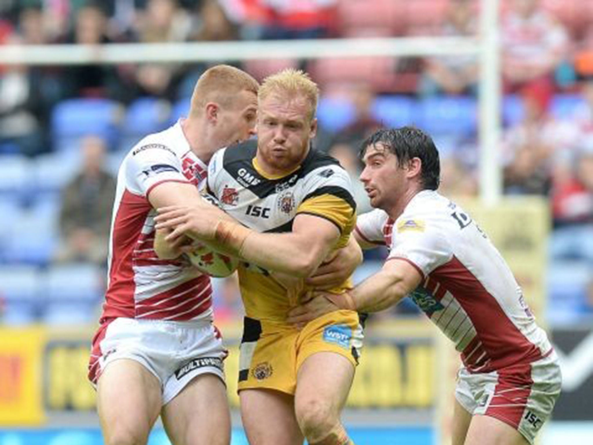 Castleford Tigers' Oliver Holmes is tackled by Wigan Warriors Jack Hughes (left) and Matty Smith (right) during the Tetley's Challenge Cup Quarter Final match at the DW Stadium, Wigan.