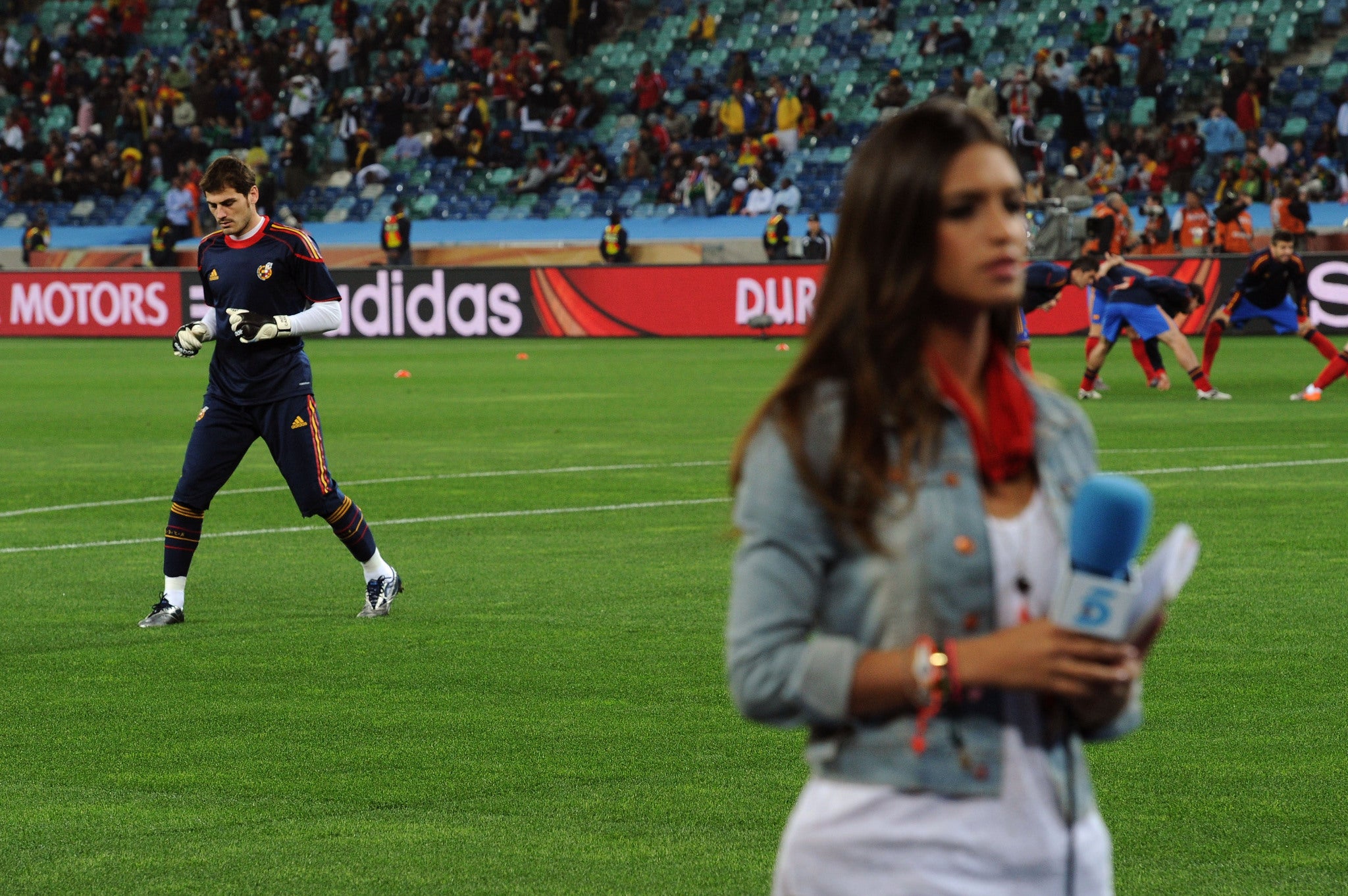 Journalist Sara Carbonero prepares a piece to camera while her partner Iker Cassillas warms up