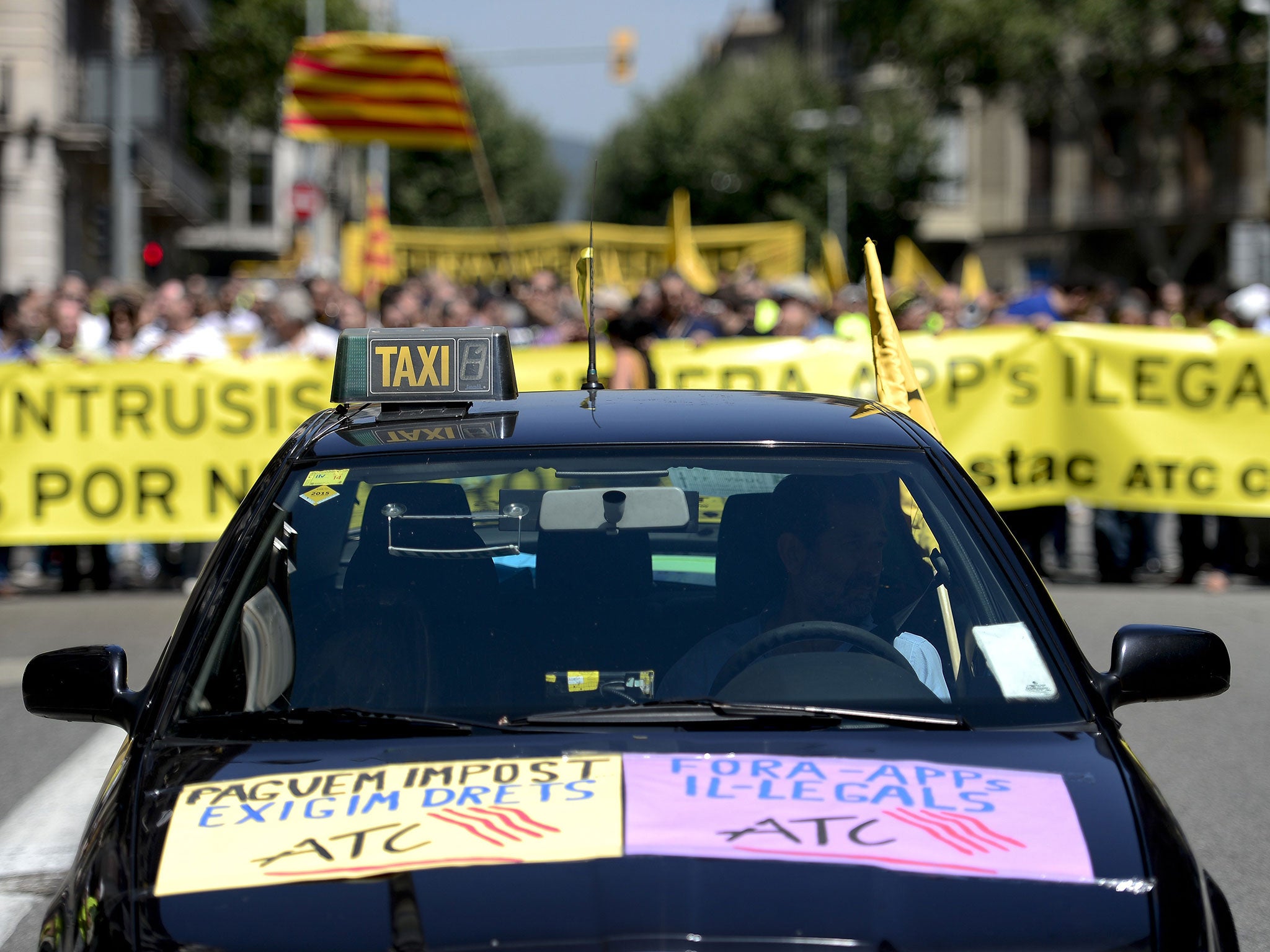 A taxi proceeds demonstrators holding a banner during a strike action in protest of unliscensed taxi-type-services in Barcelona