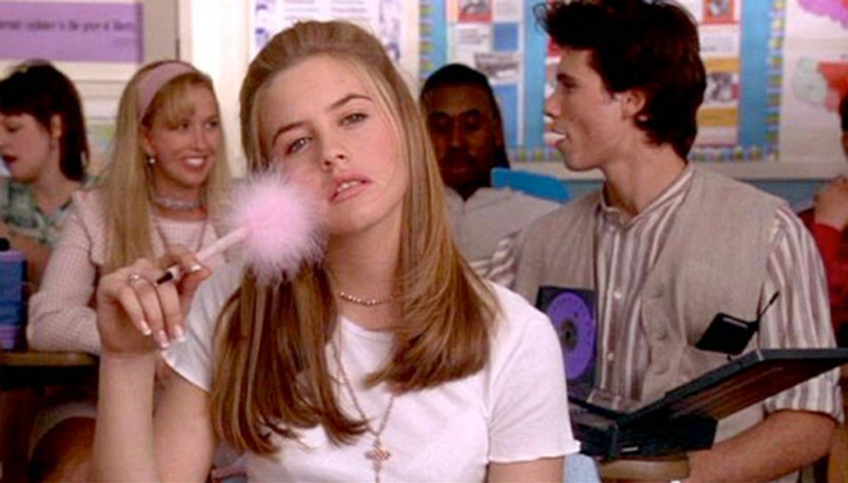 Image is from the film 'Clueless' (1995). In a high school classroom, Cher daydreams with a fluffy, pink pen pressed to her cheek.