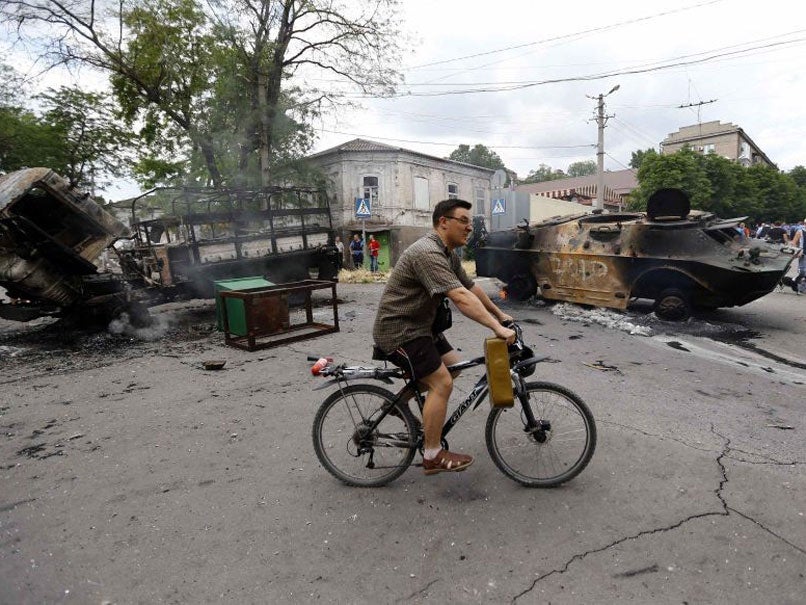 A resident cycles past destroyed vehicles at the site of fighting in the eastern Ukrainian port city of Mariupol June 13, 2014.