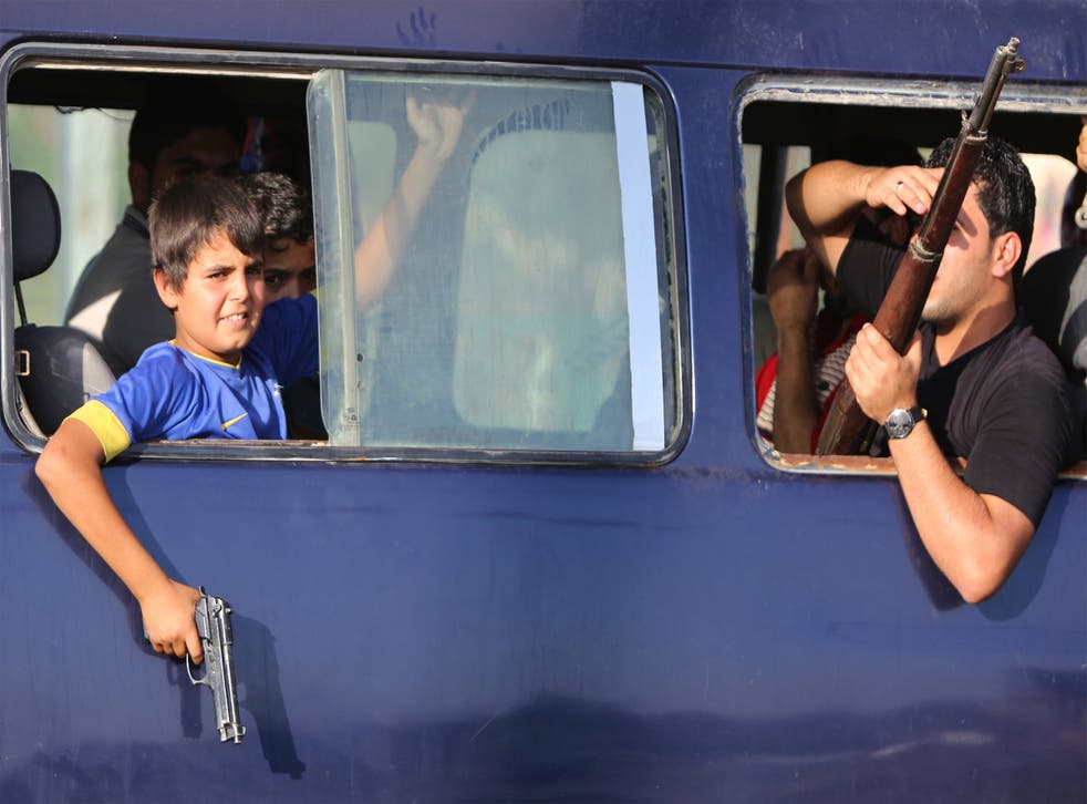 An Iraqi young boy holds a gun from the window of a vehicle carrying volunteers joining Iraqi security forces