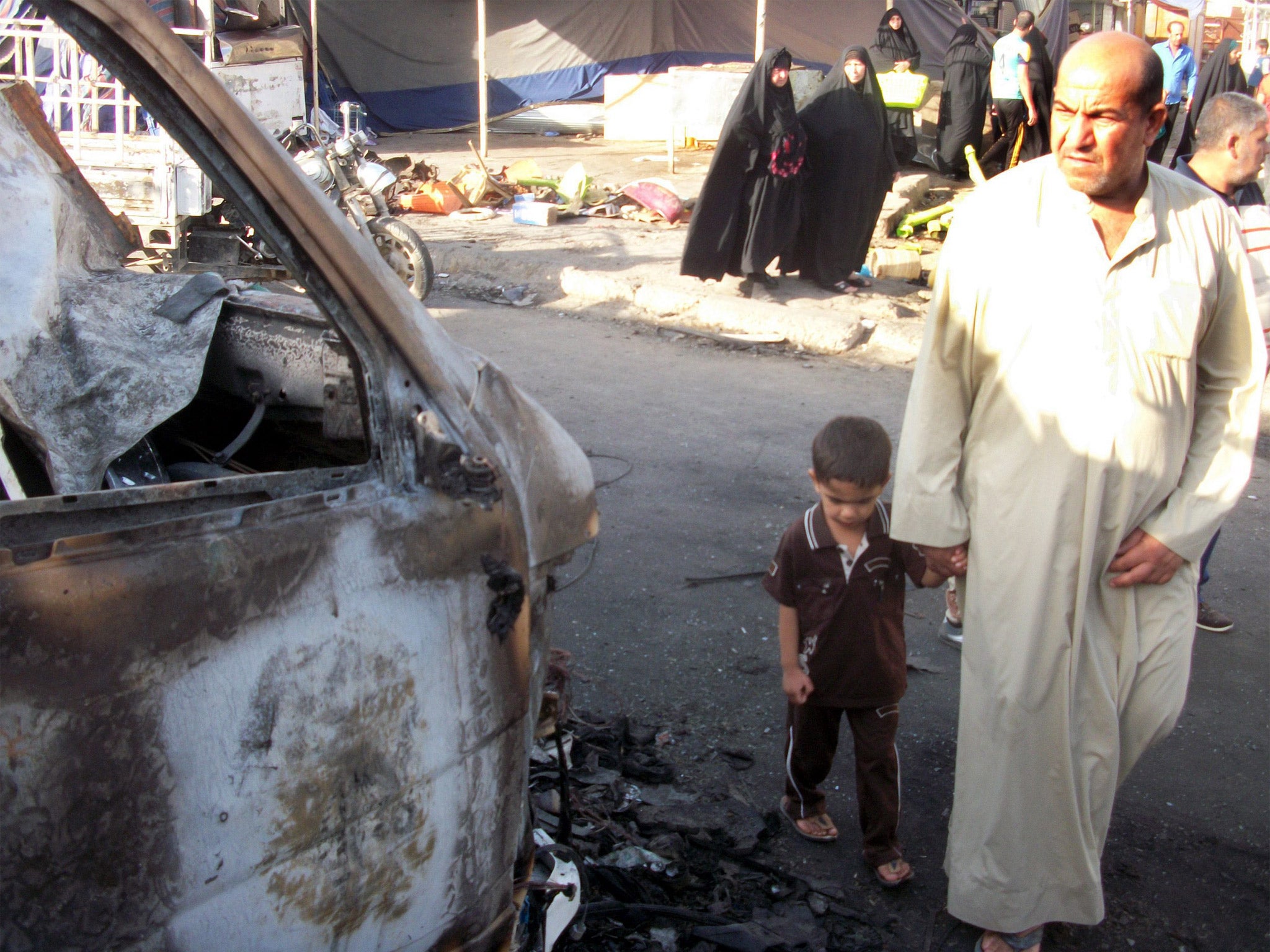 An Iraqi man with a boy inspects the scene of a car bomb attack in Sadr city