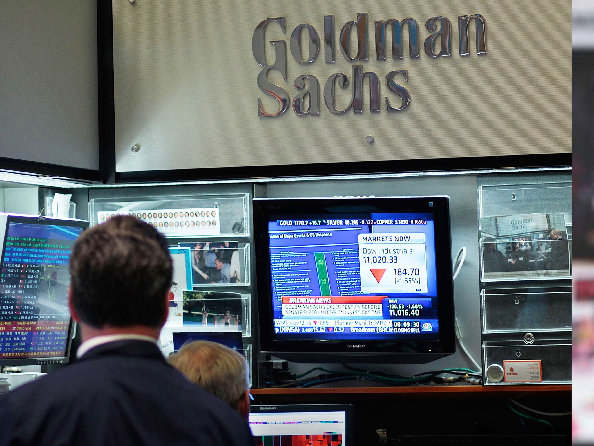 Traders sit in the Goldman Sachs booth on the floor of the New York Stock Exchange watch a television showing market news