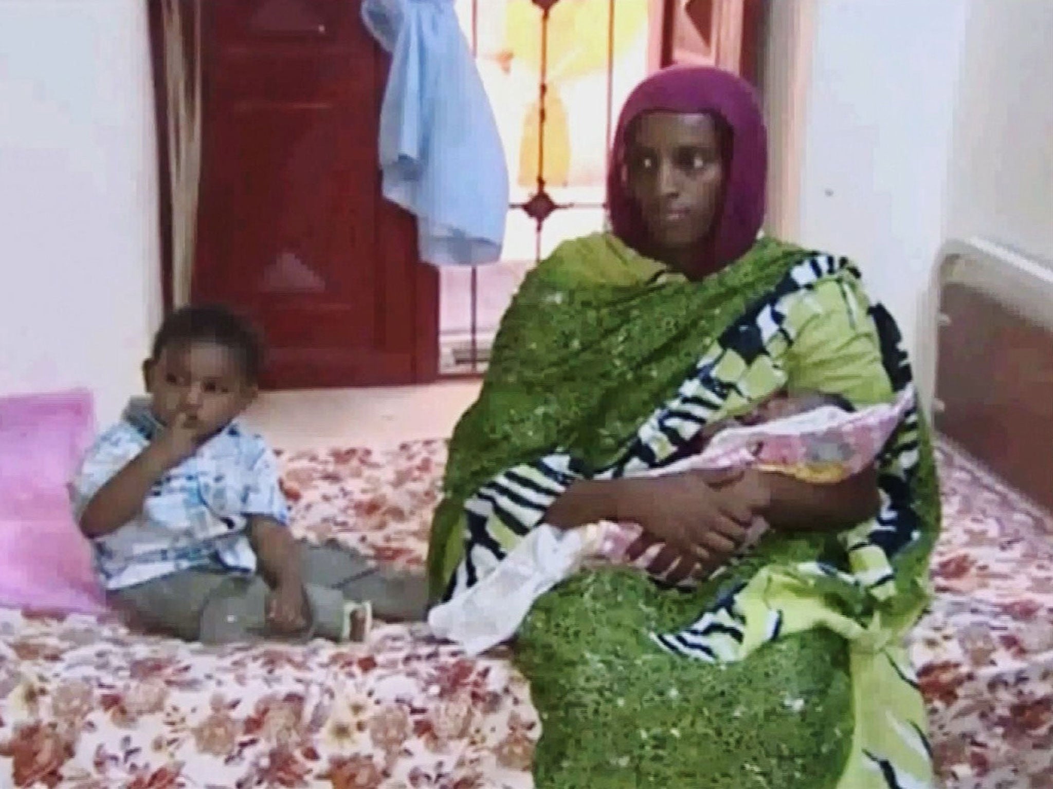 In this file image from an undated video Meriam Ibrahim, sitting next to her 18-month-old son Martin, holds her newborn baby girl as an NGO visits her in a room at a prison in Khartoum