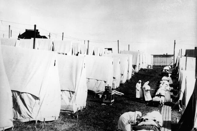 Masked doctors and nurses treat flu patients lying on cots and in outdoor tents at a hospital camp during the influenza epidemic of 1918 