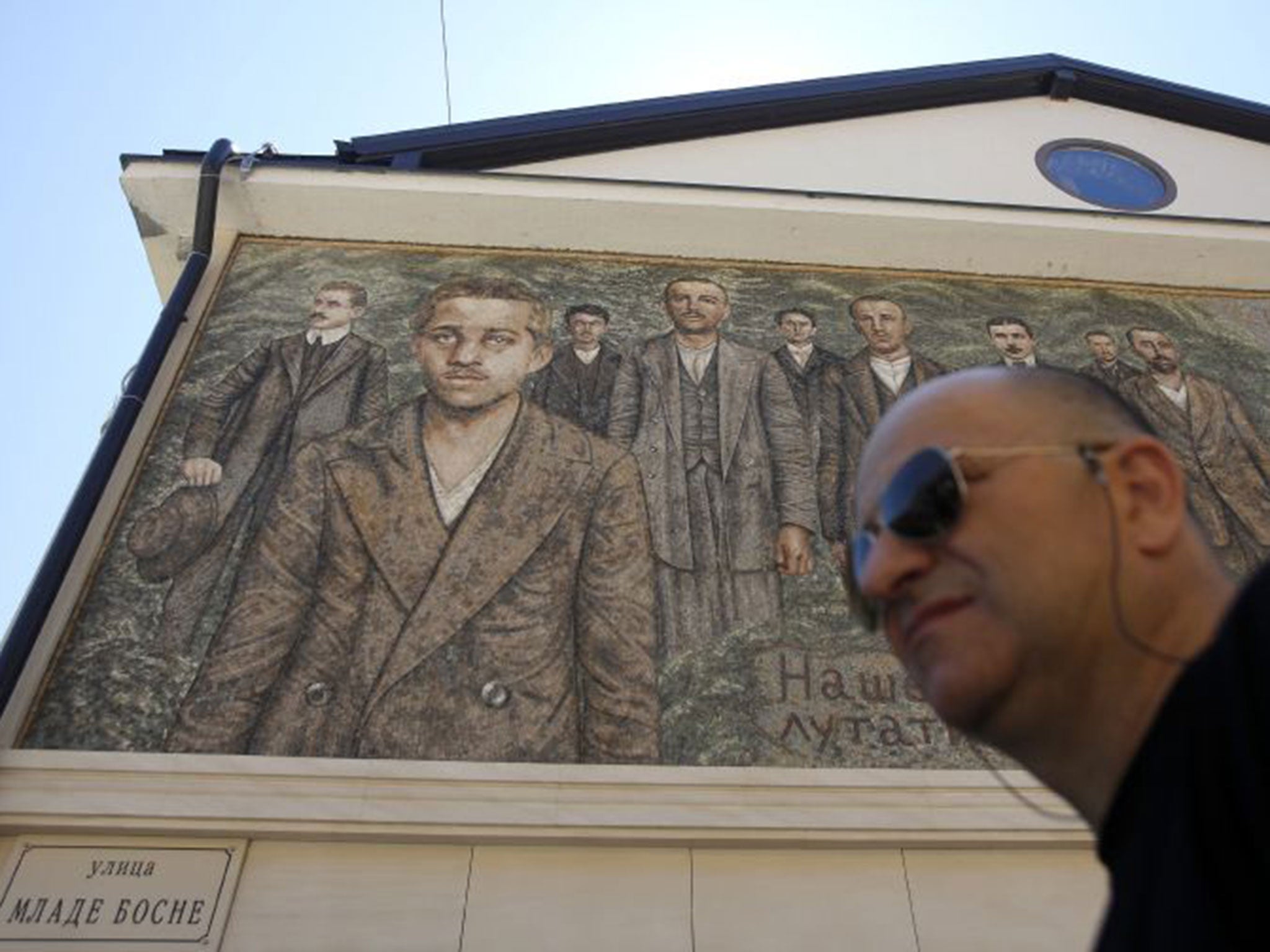 A man walks by a mosaic depicting assassin Gavrilo Princip, in Visegrad