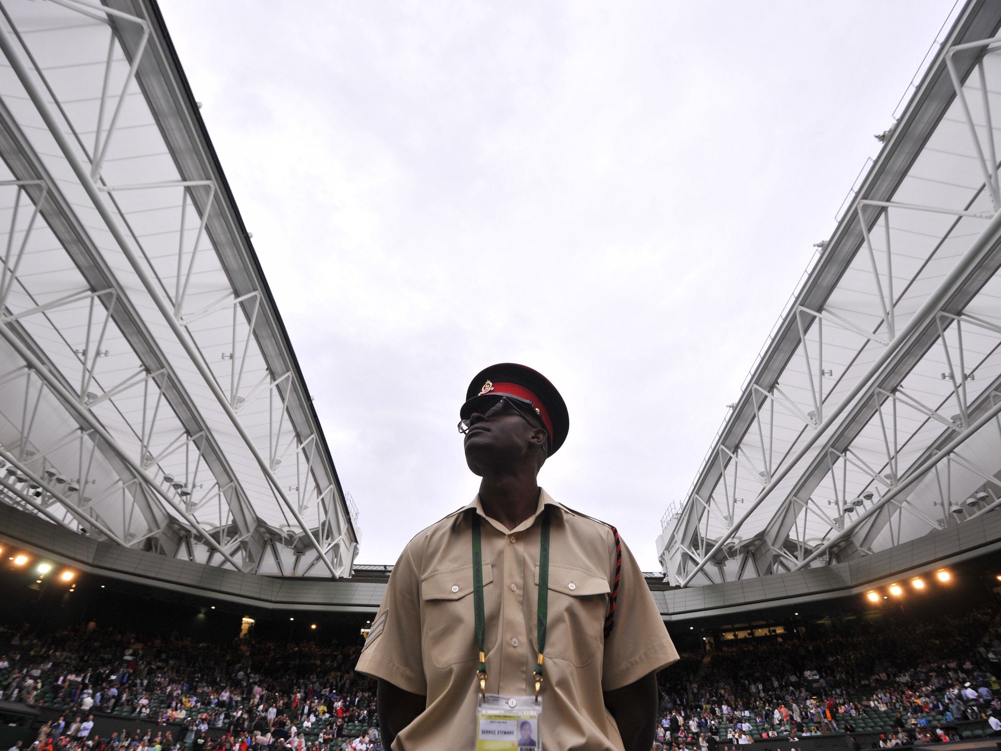 Caption:A security guard looks on as the roof on Centre Court is closed against the rain.