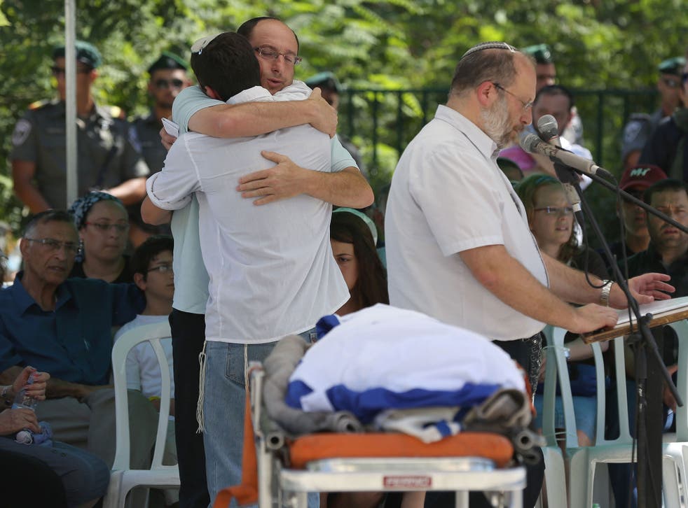 Ofir, the father of Gilad Shaer, 16, hugs a mourner as they stand in front of his son's body during a funeral service at his hometown, the Talmon Jewish settlement, near the West Bank city of Ramallah