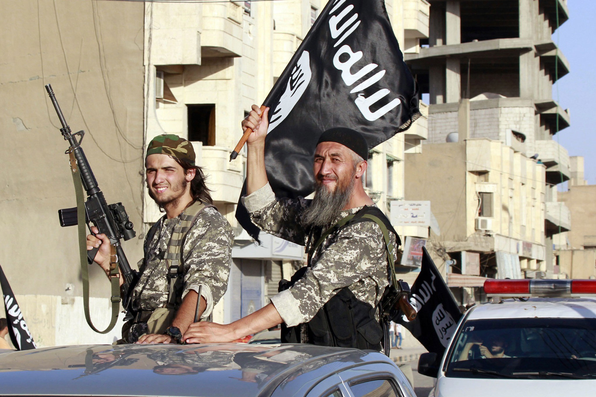 Isis fighters wave flags as they take part in a military parade along the streets of Syria's northern Raqqa province