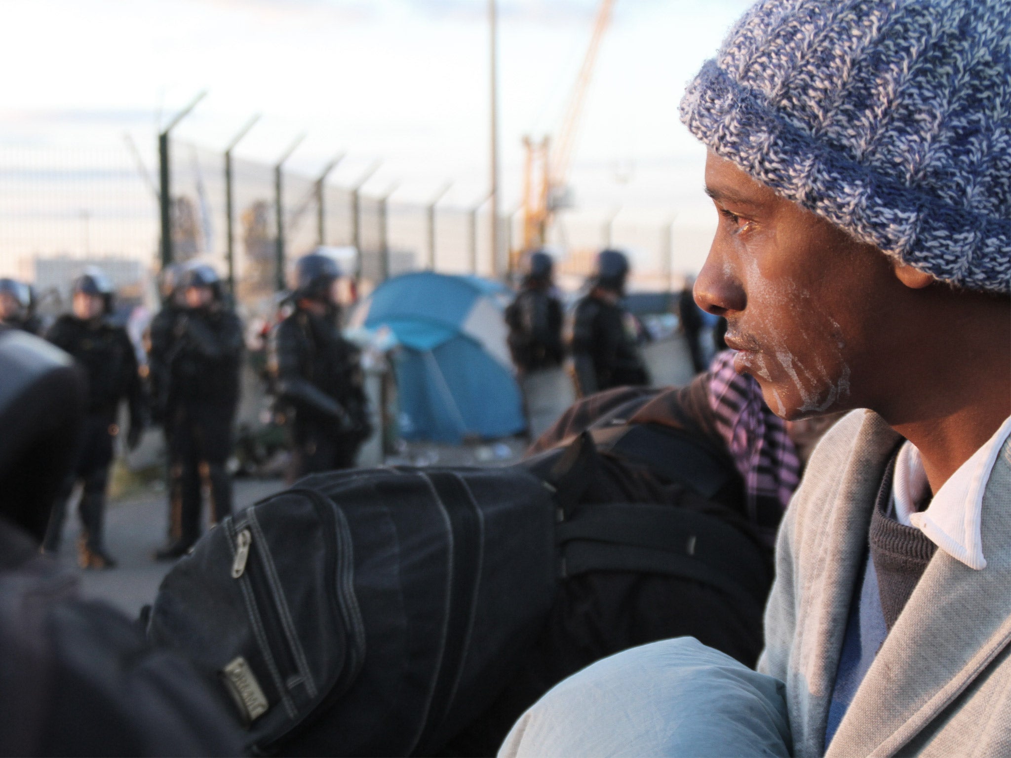 A migrant, his face streaked with the after-effects of tear gas, awaits transportation to a detention centre following the clearance of a camp in Calais