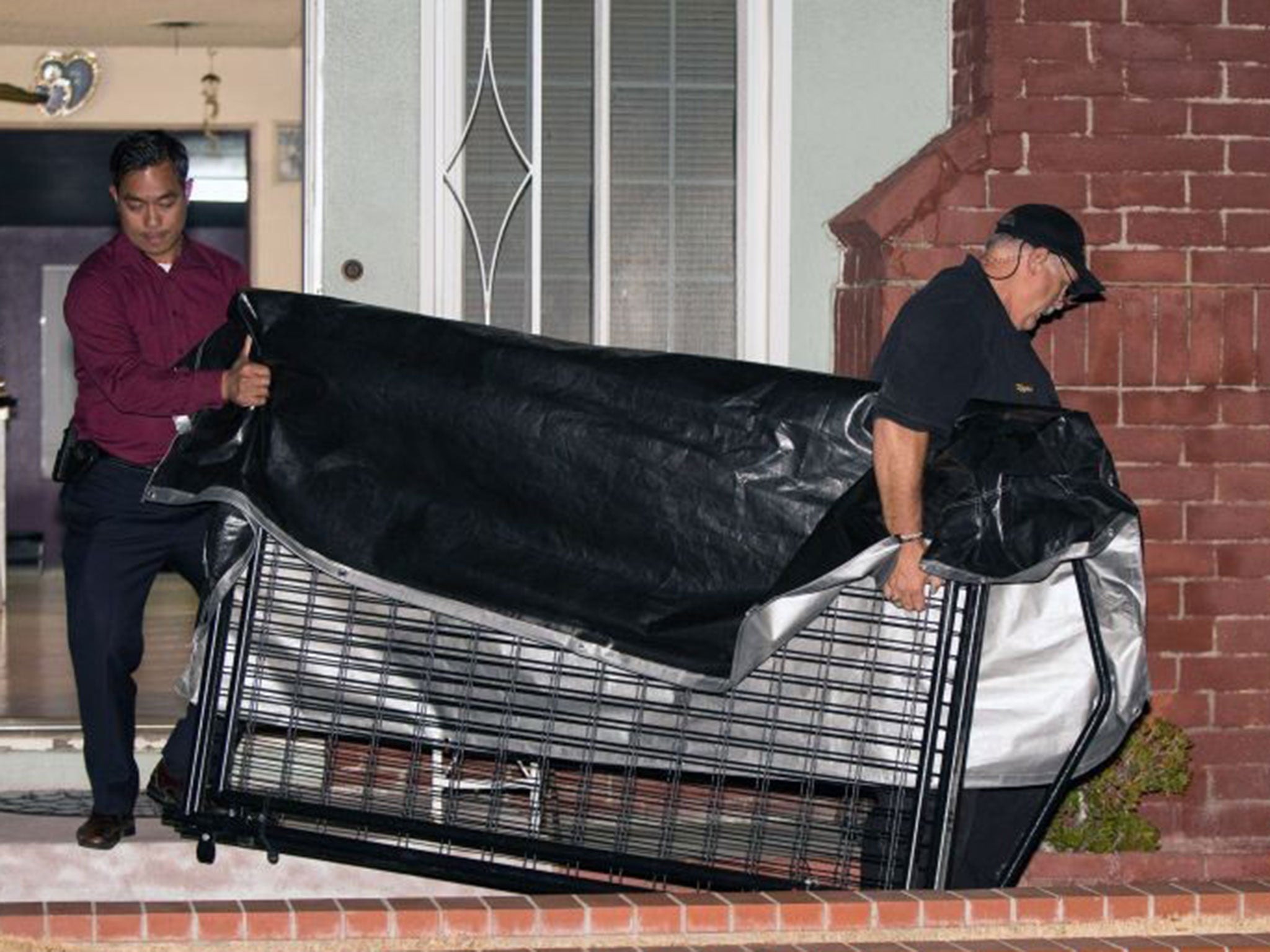 In this Tuesday, July 1, 2014 photo, a crime scene investigator and a detective carry a cage from a residence in Anaheim, Calif. An 11-year-old autistic boy who police suspect was kept in a cage has been removed from the home, and his parents have been ar
