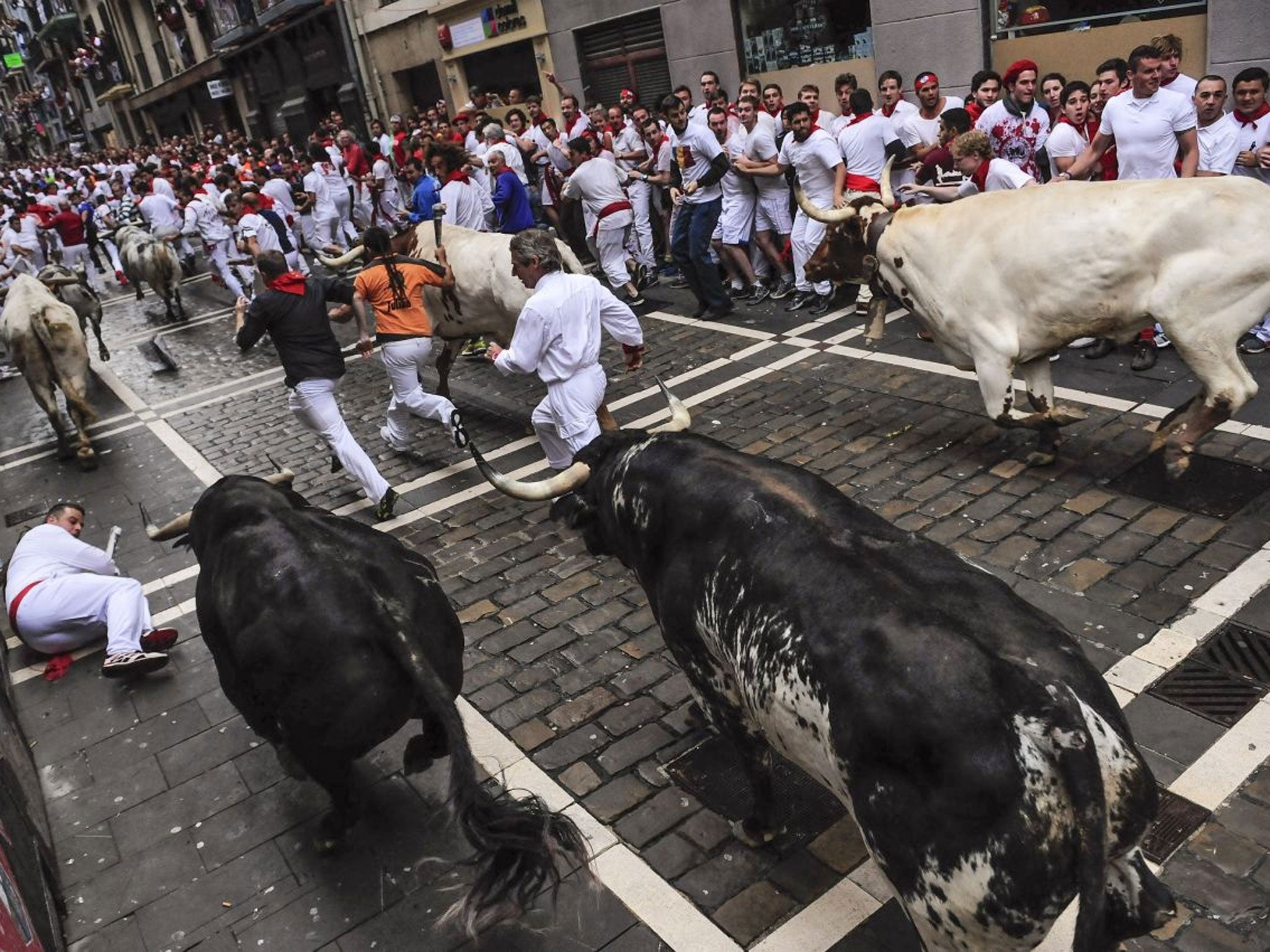 Revelers run ahead of fighting bulls on Estafeta corner during the running of the bulls at the San Fermin festival, in Pamplona, Spain